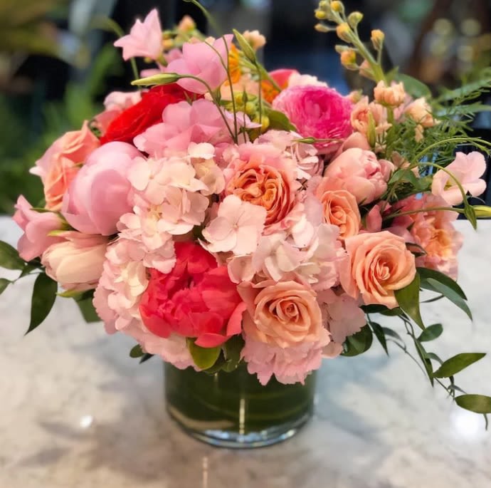 Velours Pêche - Indulge in the soft romance and refined luxury of &quot;Velours Pêche&quot;, a breathtaking floral arrangement designed to capture the warmth and elegance of a golden sunset. This Valentine’s Day, express your deepest sentiments with this lush combination of peach garden roses, delicate peonies, hydrangeas, and ranunculus, expertly arranged in a sleek glass vase to create a harmonious and radiant display.  The blush and coral tones symbolize adoration, sincerity, and heartfelt connection, while the wisps of fresh greenery add a natural and organic touch. Each bloom is carefully selected for its delicate texture and timeless beauty, making this luxurious arrangement the perfect way to celebrate love, romance, and unforgettable moments.  With its rich, peach-infused hues and elegant composition, &quot;Velours Pêche&quot; is a sophisticated floral statement, ensuring an unparalleled and luxurious gifting experience.  Dimensions: Approx. 14&quot; high x 14&quot; wide  #Luxury Peach Floral Arrangement #Elegant Hydrangea and Peony Bouquet #Premium Valentine’s Flowers #Sophisticated Romantic Centerpiece #High-End Coral and Blush Roses