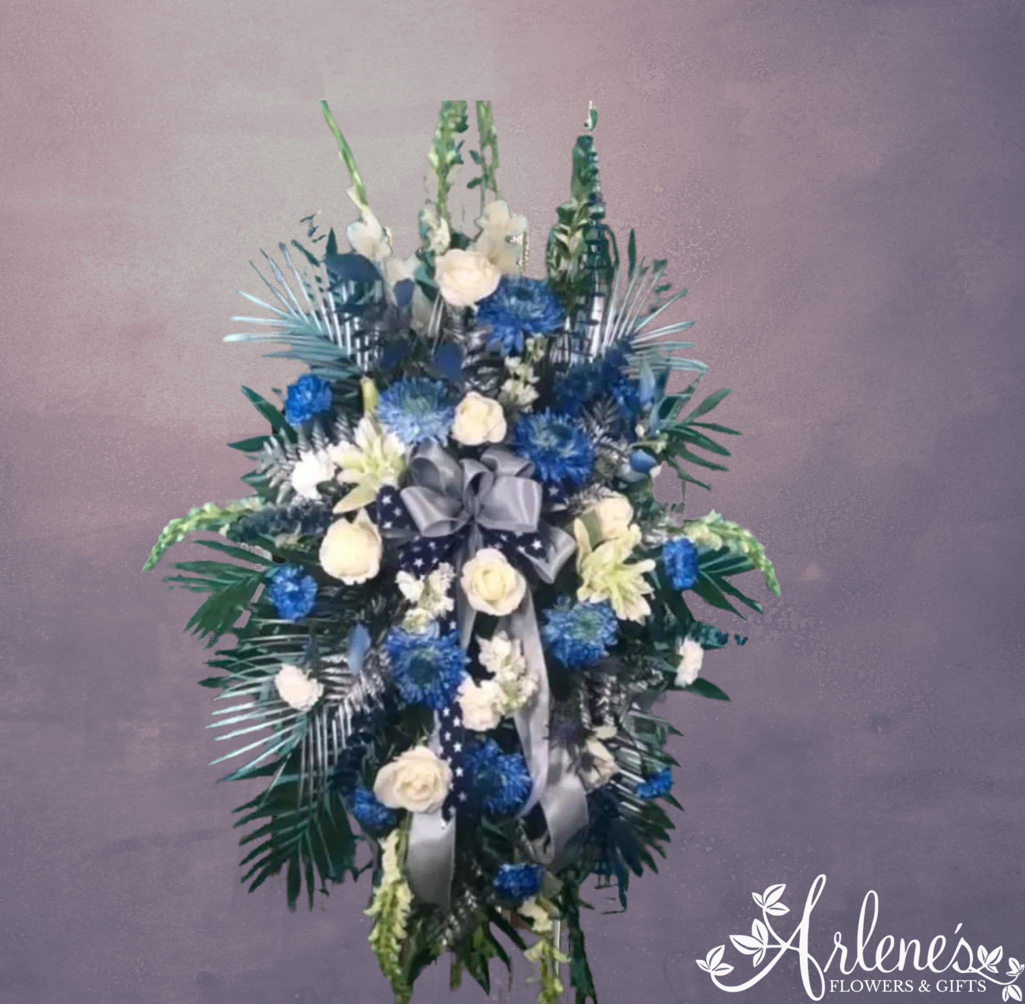 Final Field Goal Standing Spray - This blue, silver and white spray stands to memorialize devotion to our favorite football team. We get this request quite often, and wanted to show some examples, no singular flower type is guaranteed in this style of spray, but it will be full and beautiful!  If you have any of your fallen fan's memorabilia you would like included in the spray, please call us to see if this would be a possibility to incorporate into the design (footballs, signs, etc.). We love to customize and make it unique for y'all.