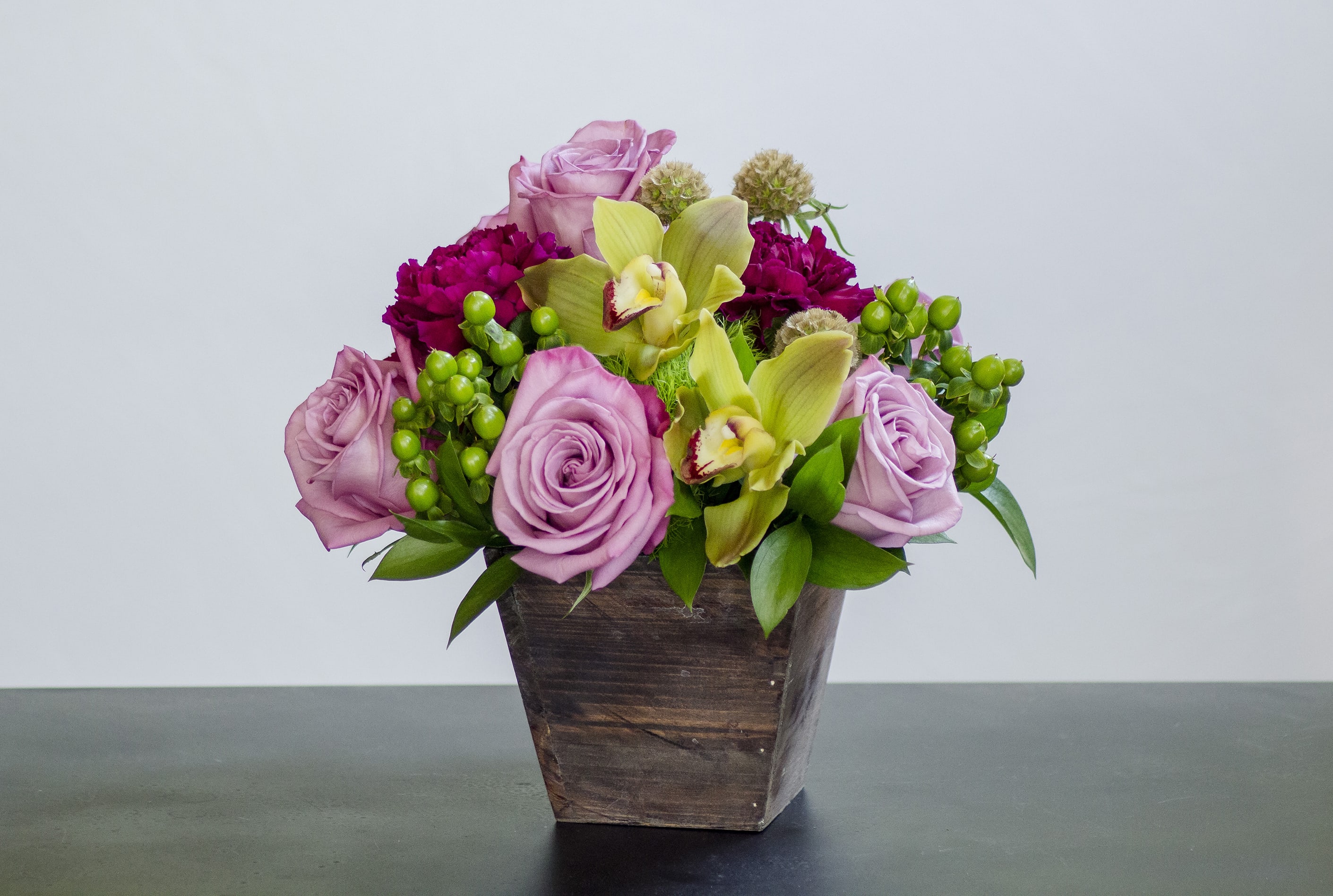Rustic Elegance by Garden Gate Floral Rustic Elegance by Garden Gate Floral - This is a simple rustic style arrangement with pops of class and elegance. It's perfect for any occasion and anyone! This arrangement includes, moody blue roses, plum carnations, green cymbidium orchids, green dianthus, green hypericum berries, and scabiosa pods.