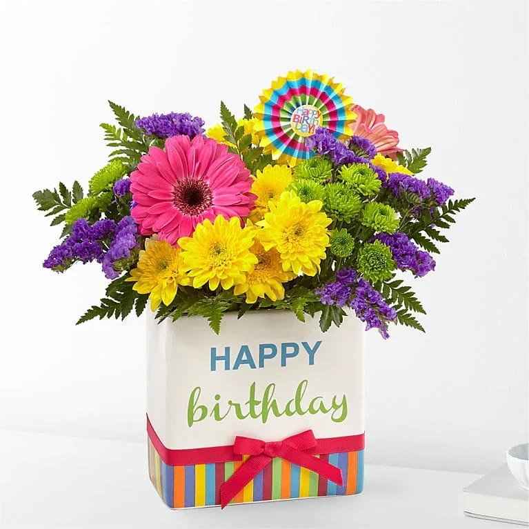Hooray! It's Your Birthday! - Our &quot;Hooray! It's Your Birthday!&quot; Bouquet is a true celebration of color and life to surprise and delight your special recipient on their big day!  Vibrantly colored gerbera daisies (bold colorful roses are added in the Deluxe and Premium size) take center stage, surrounded by purple statice, yellow cushion poms, green button poms, and lush greens to create a party perfect birthday display. Presented in our keepsake modern rectangular ceramic vase with colorful striping at the bottom, &quot;Happy Birthday&quot; lettering at the top, and a bright pink bow at the center, this unforgettable fresh flower arrangement is then accented with a striped happy birthday pick to create a fun and festive gift.  This happy surprise is sure to make the moment one they’ll remember.  Add a Happy Birthday balloon to make it over-the-top!