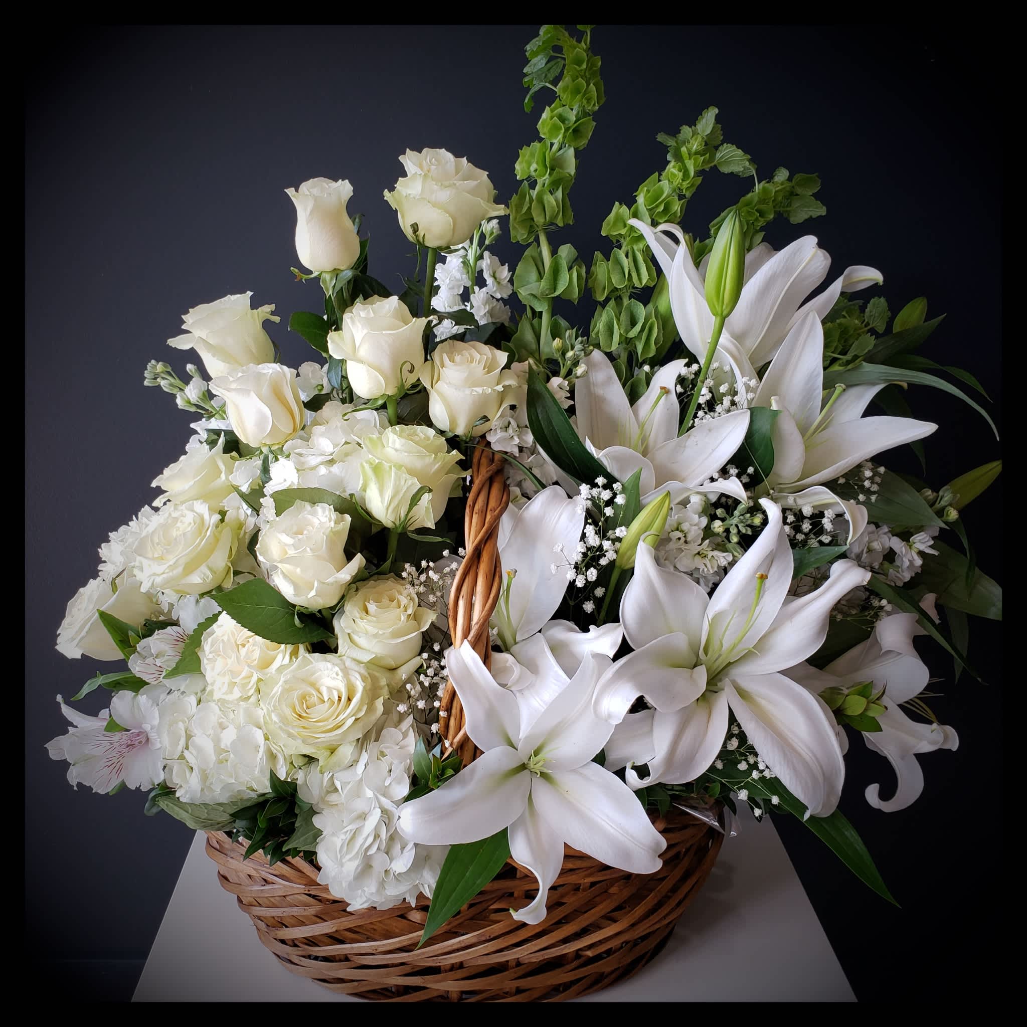 Purity Basket - An all white sympathy basket of lilies, roses, hydrangeas are accented with bells of Ireland and baby's breath.