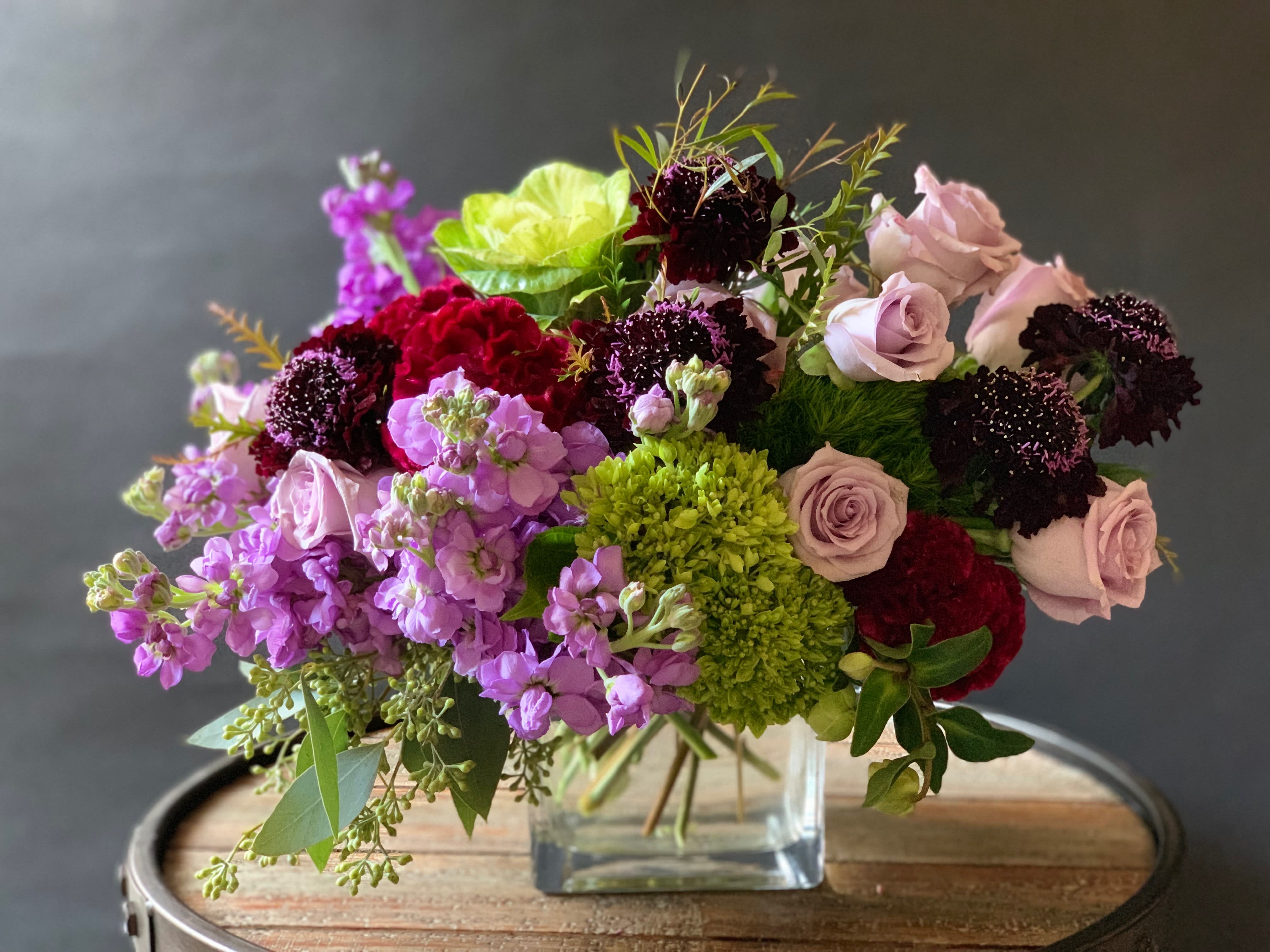 Constance - Nature's showcase, a stunning mix of interesting textures. Designed on a lush base of greens, lavenders, and burgundy it creates a perfect setup for the super stars scabiosas.  *Picture showcases our delux version.