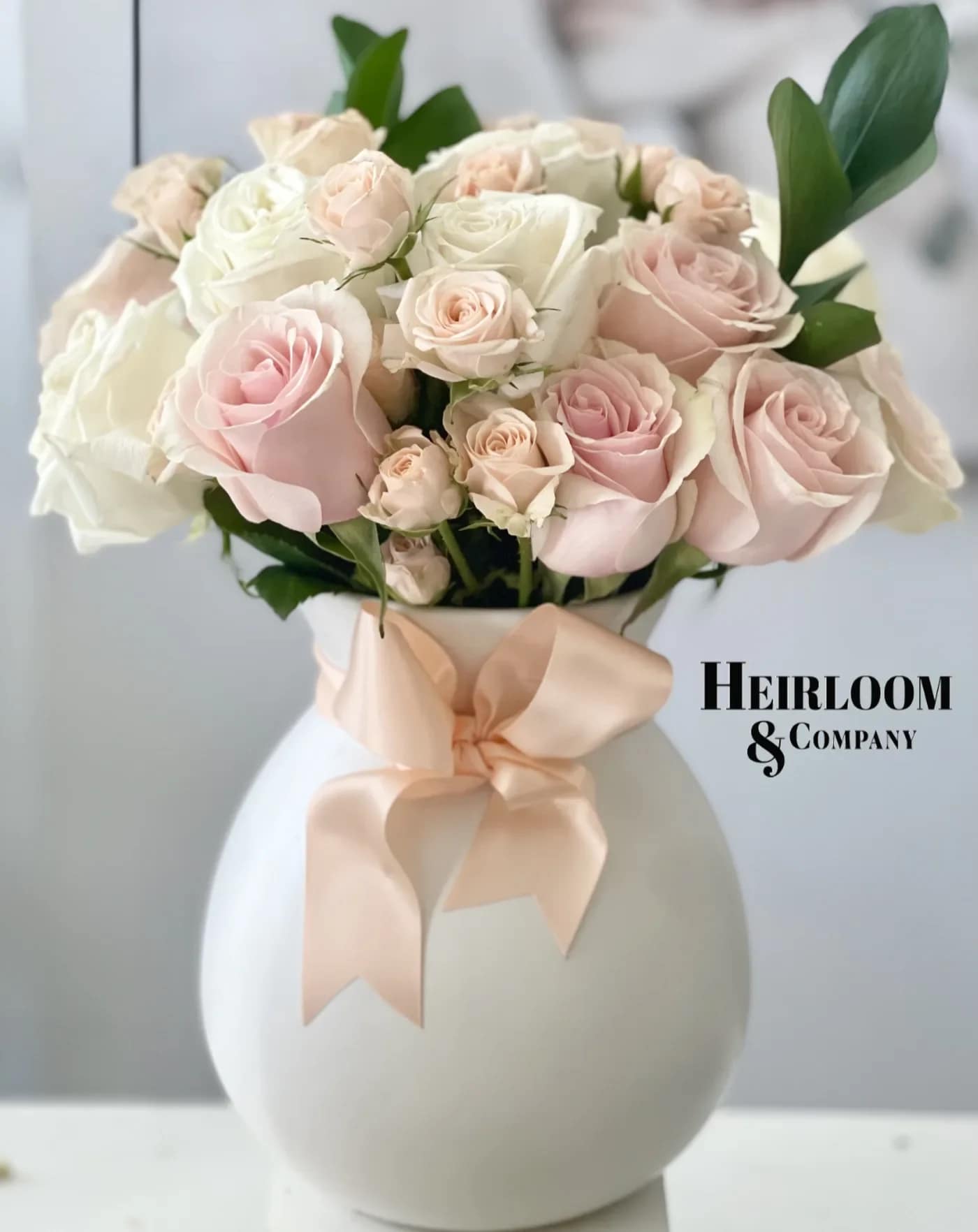 Elle Elle - Celebrate love with our Blush & Bloom arrangement, a timeless bouquet of soft pink and ivory roses nestled in lush greenery. Designed in our signature white vase and adorned with a delicate satin bow, this elegant floral piece embodies romance, grace, and heartfelt affection. Whether you’re surprising your special someone or treating yourself, this arrangement is the perfect way to express love and admiration this Valentine’s Day.