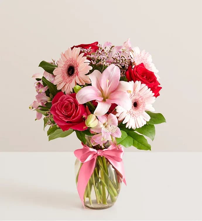Fields Of Europe® Romance - Inspired by the rich beauty of the European countryside, our romantic bouquet reveals all the feelings you have in your heart. Fresh-picked pink &amp; red blooms are on display inside a glass vase finished with ribbon, creating a timeless gift for someone you love. All-around arrangement with red and hot pink roses, pink Asiatic lilies, Peruvian lilies (alstroemeria), Gerbera daisies and limonium; accented with assorted greenery Artistically designed in a clear glass vase accented with a pink satin ribbon