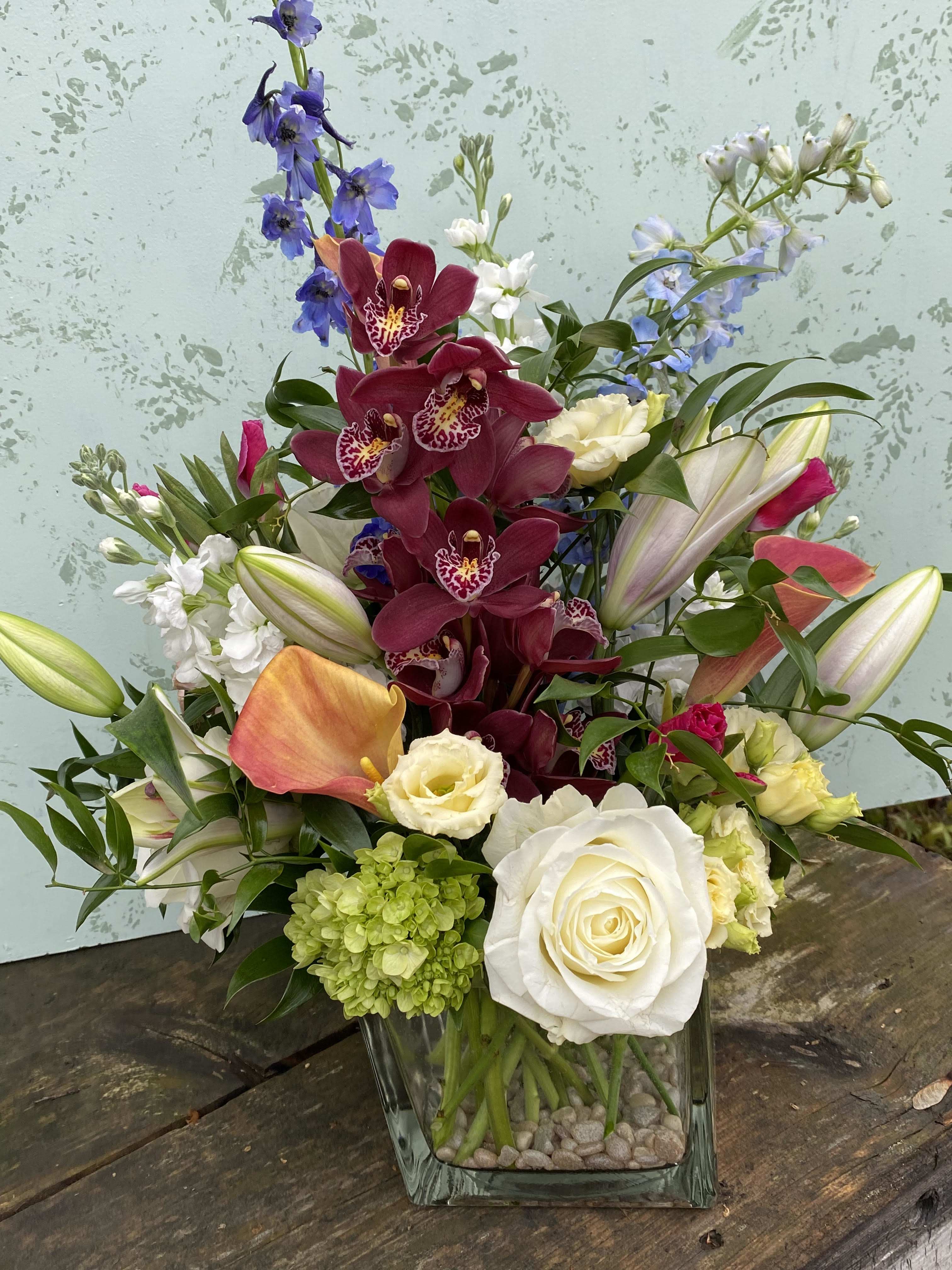 Orchid surprise - Vase arrangement designed with delphinium, orchids, stock, roses, calla lily, and hydrangea, in a square glass vase. 