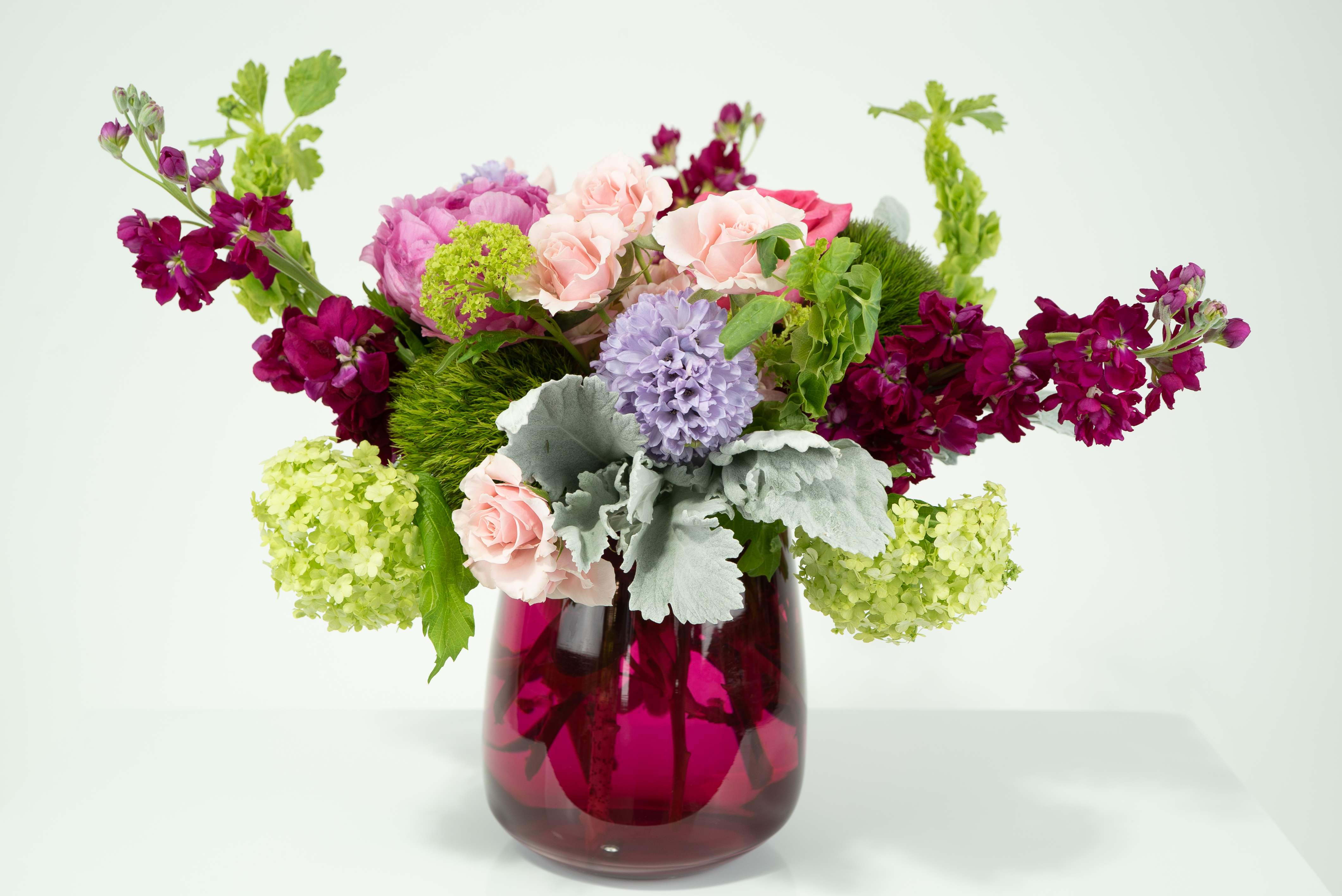 Confection Confection - This sweet sweet bunch of flowers, if it were a candy would make your mouth water. It is adorned with hot pink roses, spray roses, hyacinth, viburnum, dianthus, stock, peony, bells of ireland and dusty miller.