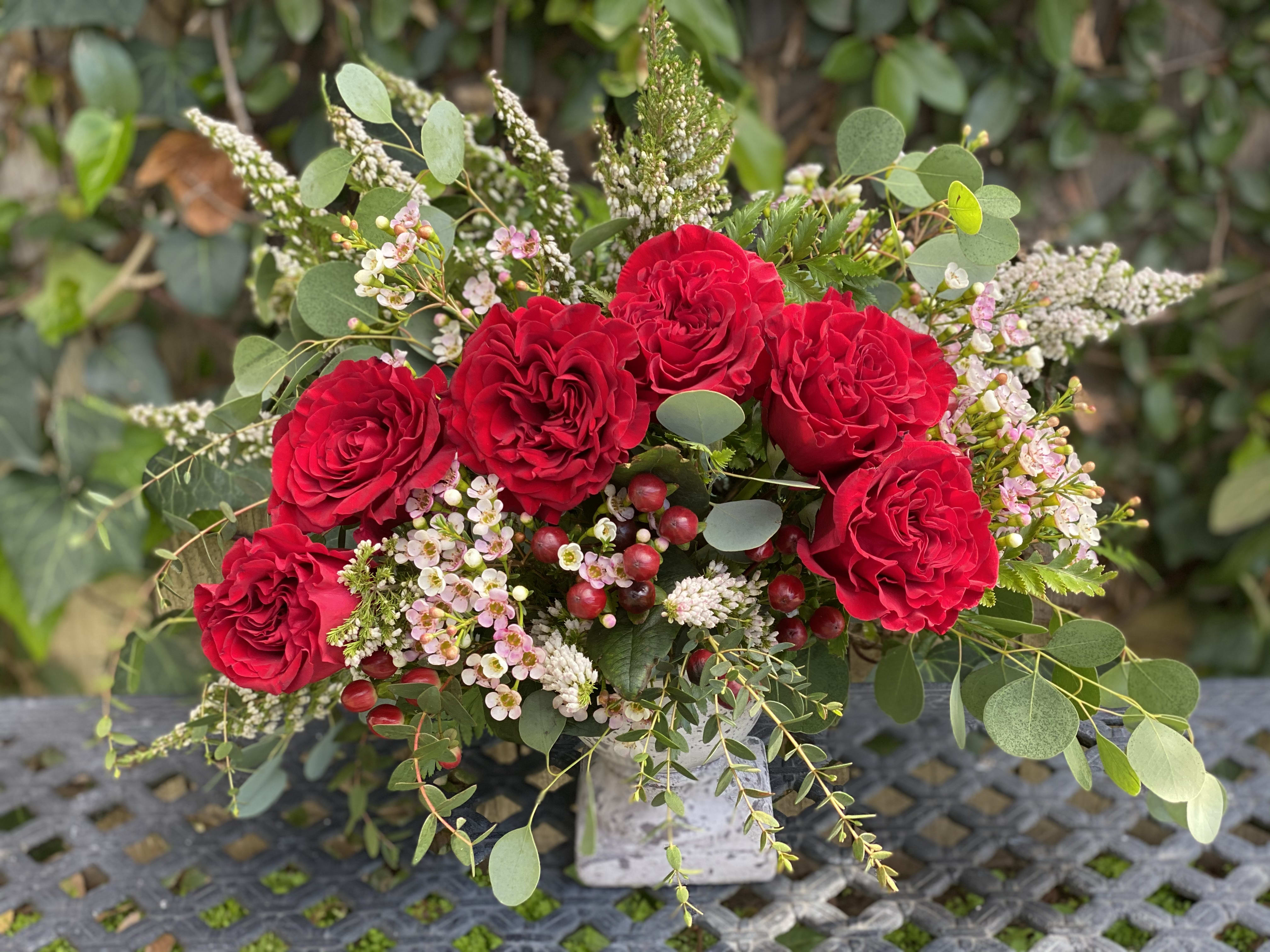 Amante  - The subtle holiday design is perfect for seasonal decor. With vibrant red roses and touches of fragrant eucalyptus, arranged in a classic stone vase that will make anyone feel special. 
