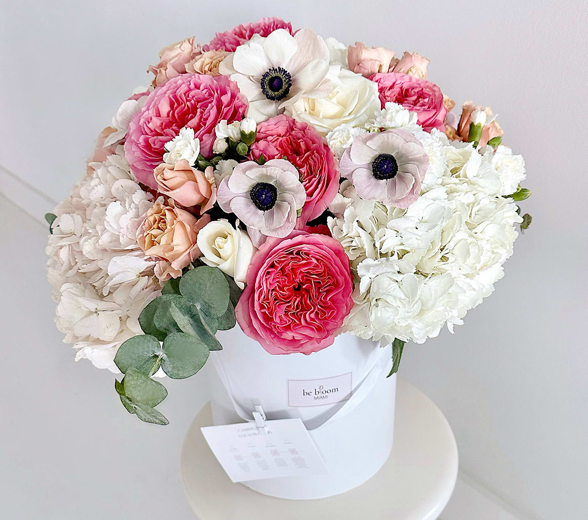Grand Radiant O'Hara Roses Blossom Box - The &quot;Grand Radiant Blossom Box&quot; is more than a floral arrangement—it's an experience. At first glance, your eyes are drawn to the striking hot pink O'Hara roses, a symbol of bold love and appreciation. They're tenderly complemented by the soft hues of peach garden roses, embodying gentle affection. As you delve deeper, the pristine purity of white hydrangeas and carnations whispers tales of innocence and new beginnings. The delicate white anemones with their dark centers add a touch of sophistication, making it a fitting gesture for various moments—from celebrations to heartfelt consolations. Interspersed with the calming scent of eucalyptus, each bloom is handpicked and arranged with precision by our seasoned florists. Presented in our luxurious signature white box, this arrangement is a celebration of craftsmanship and nature's beauty. Whether marking a milestone, expressing gratitude, or simply looking to brighten someone's day, the &quot;Grand Radiant Blossom Box&quot; speaks when words fall short. Ideal for those grand gestures when only the best will suffice.  Arrangement Details: Main Flowers: Hot pink O'Hara roses, peach garden roses, white hydrangeas, white carnations, white anemones Accents: Eucalyptus Container: Luxurious white signature box Approximate Dimensions: 12&quot;D x 14&quot;H