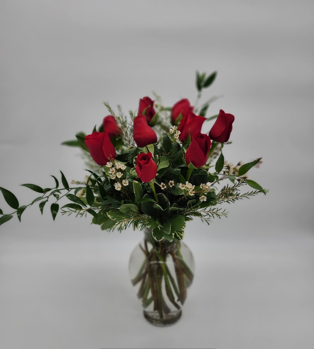 Kiss of the Rose Kiss of the Rose - Eight ravishing red roses mixed with a luxurious filler a and greens are arranged in a Glass vase.
