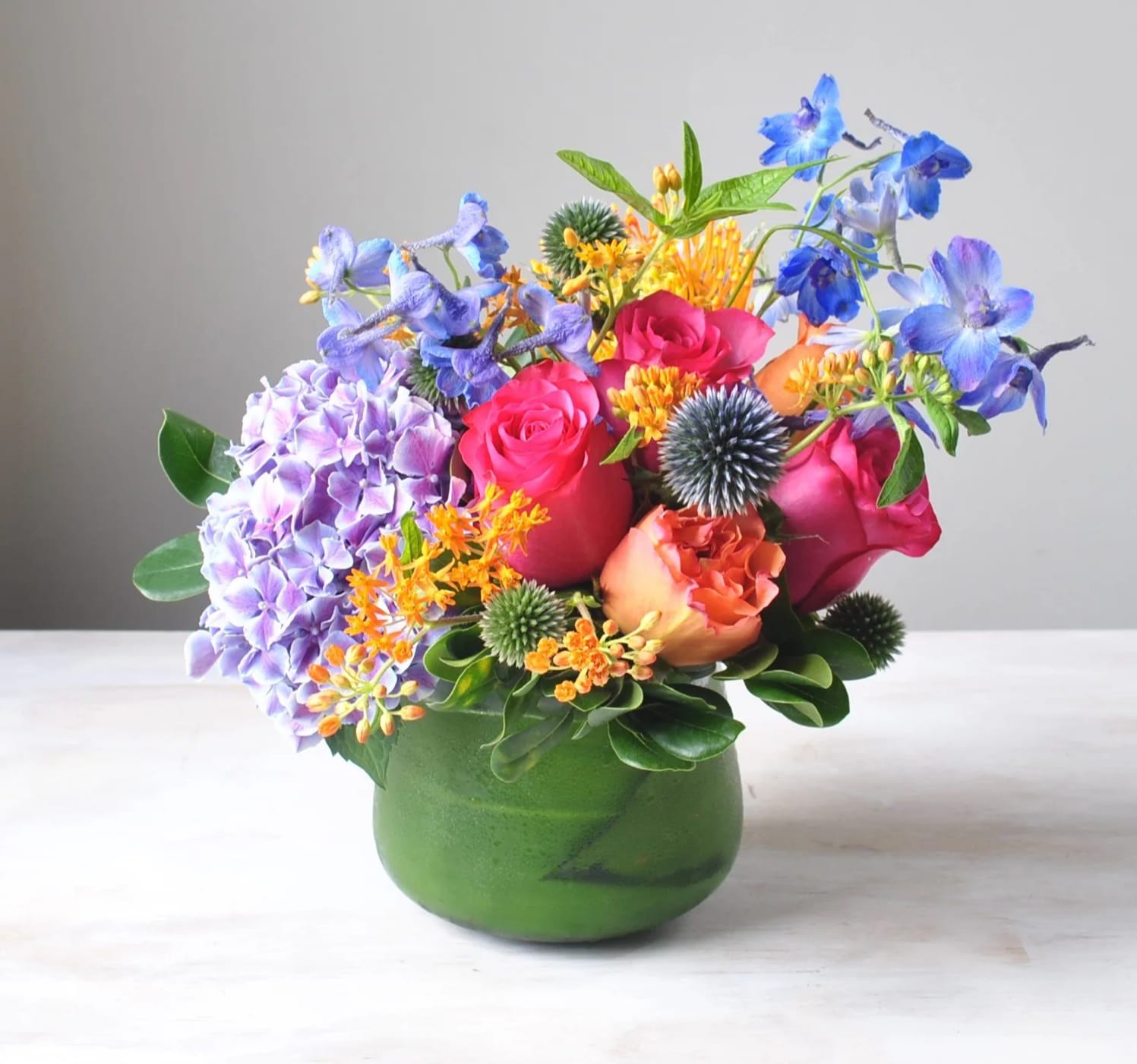Rita - Cheerful bright colors and fiery hot pink blossoms, Rita will instantly infuse energy and passion into any space. The bold, electric blue accents gracefully contrast the warm hues, adding a refreshing and unexpected twist to the arrangement. This lively ensemble is the perfect choice to brighten your recipient's day for any occasion.