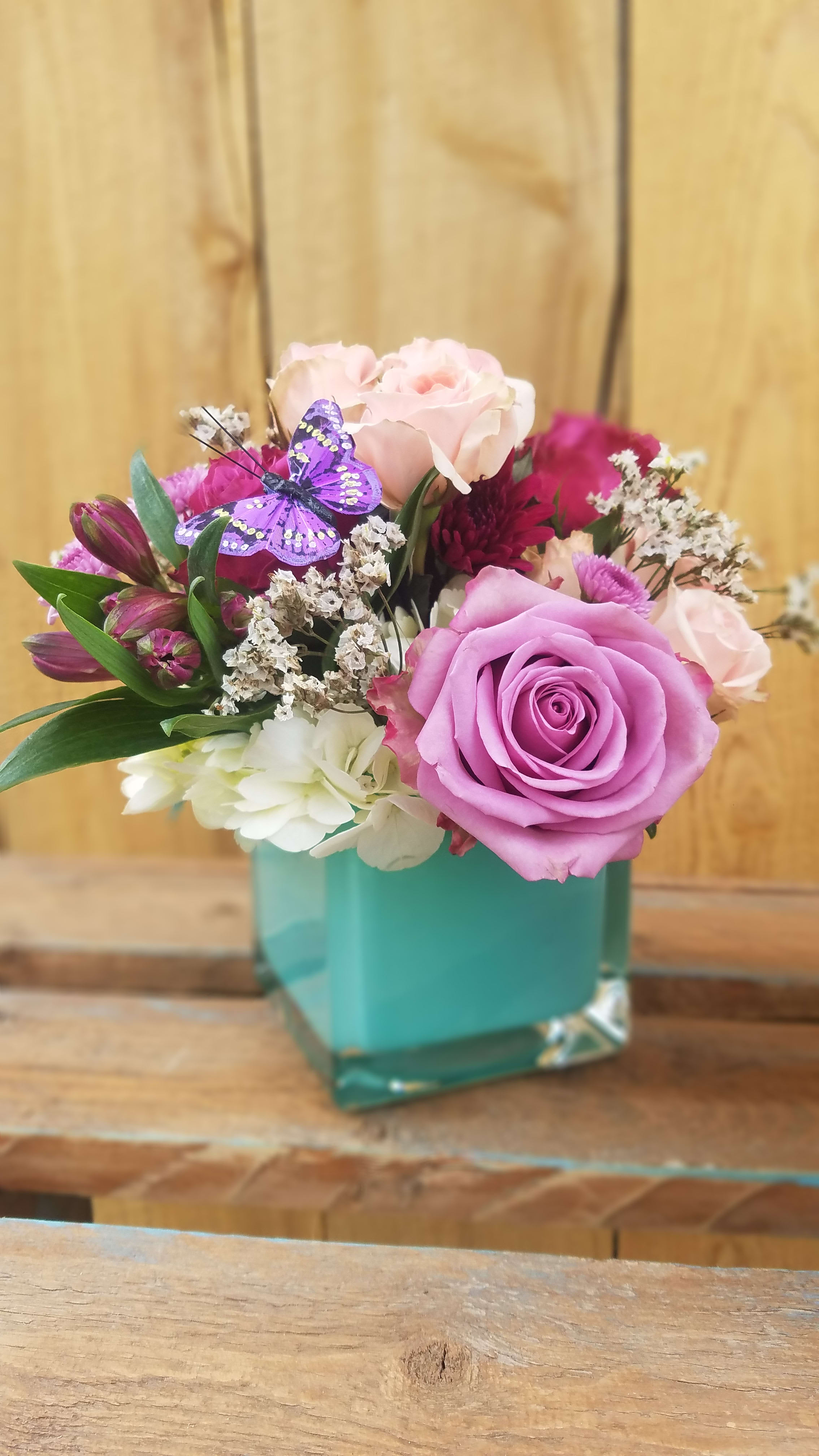 DreamScape - Assorted Colors - A colorful popular cube vase filled with lush hydrangea, roses, spray roses, alstromeria, gerber daisies, mini carnations and a sweet little silk butterfly nestled in the flowers. This arrangement is available in an assortment of color combinations. Please indicate when ordering if you would like a particular color scheme