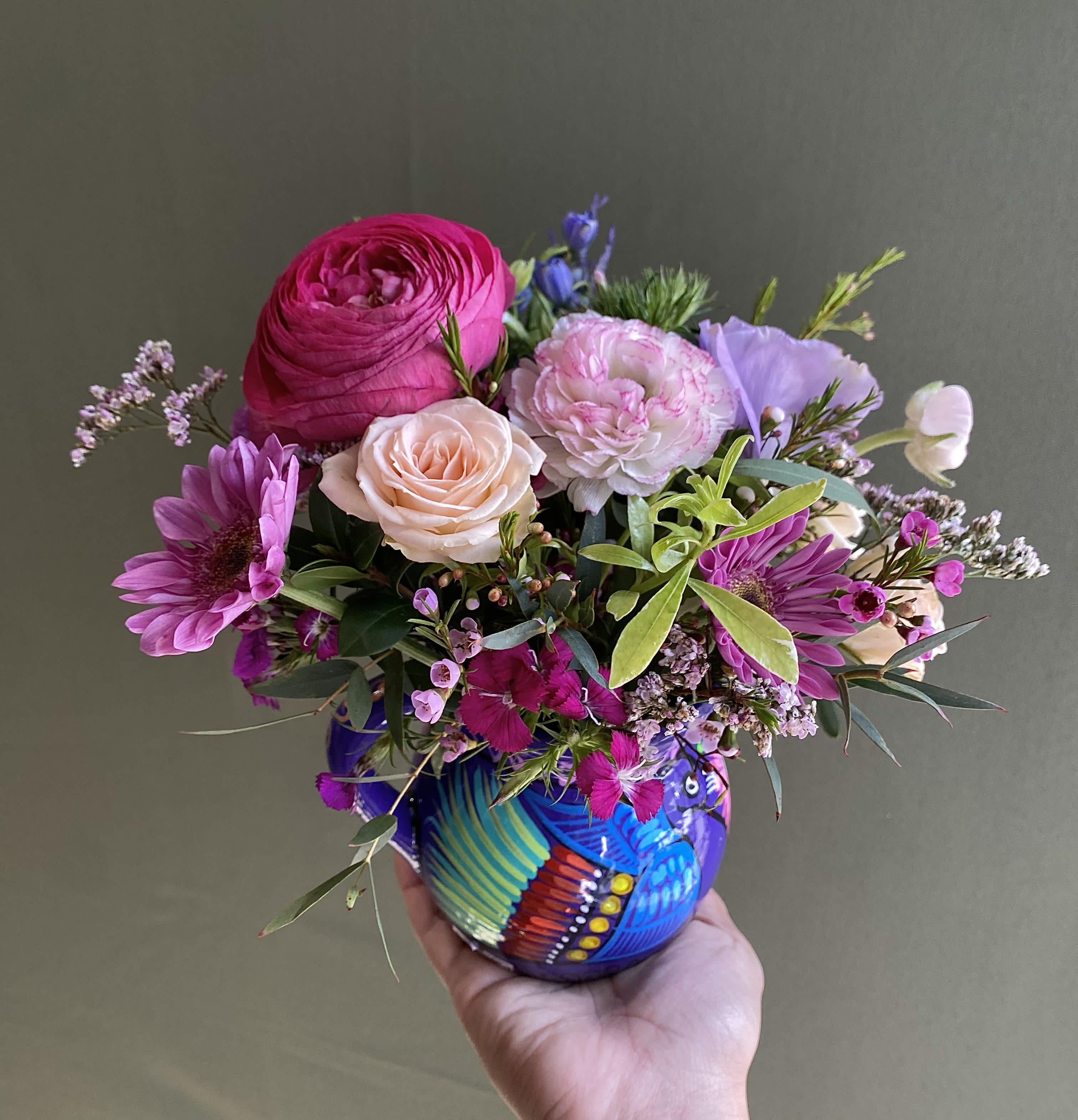 Petals Cup - An arrangement arranged in a beautiful handmade Mexican ceramic mug. Includes spray roses, lisianthus, wax flowers, ranunculus, and other filler flowers.  NOTE: The color of the mug may vary depending on availability.