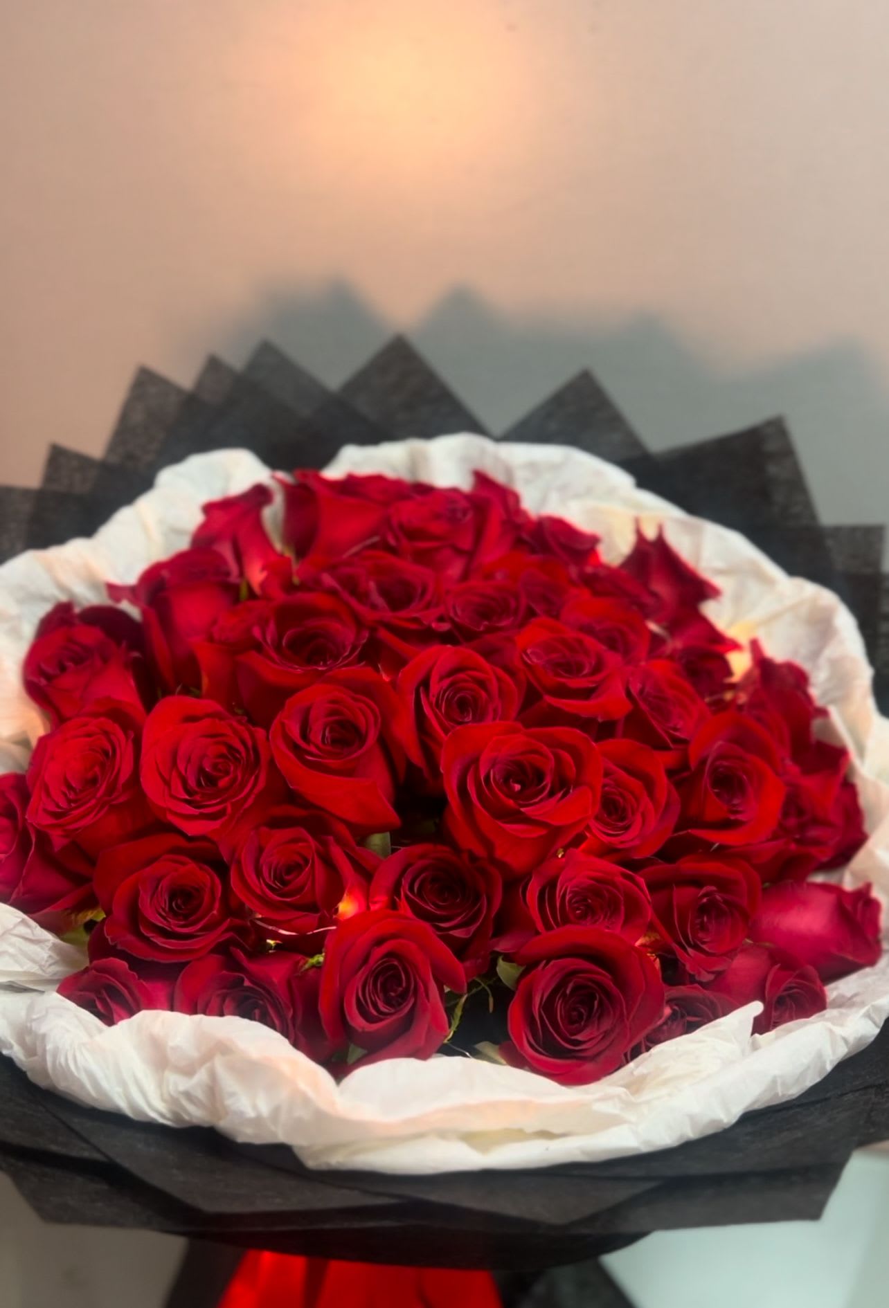 Radiant Bouquet - Description:  A luxurious bouquet of 75 deep red roses, elegantly wrapped with a striking presentation. The roses are arranged in a circular formation, creating a full and abundant look, perfect for romantic gestures, anniversaries, or special occasions. The bouquet exudes sophistication and timeless beauty.  AS SIMILAR AS POSSIBLE  Substitution based on season, flowers availability or any unforeseen or uncontrollable circumstances.