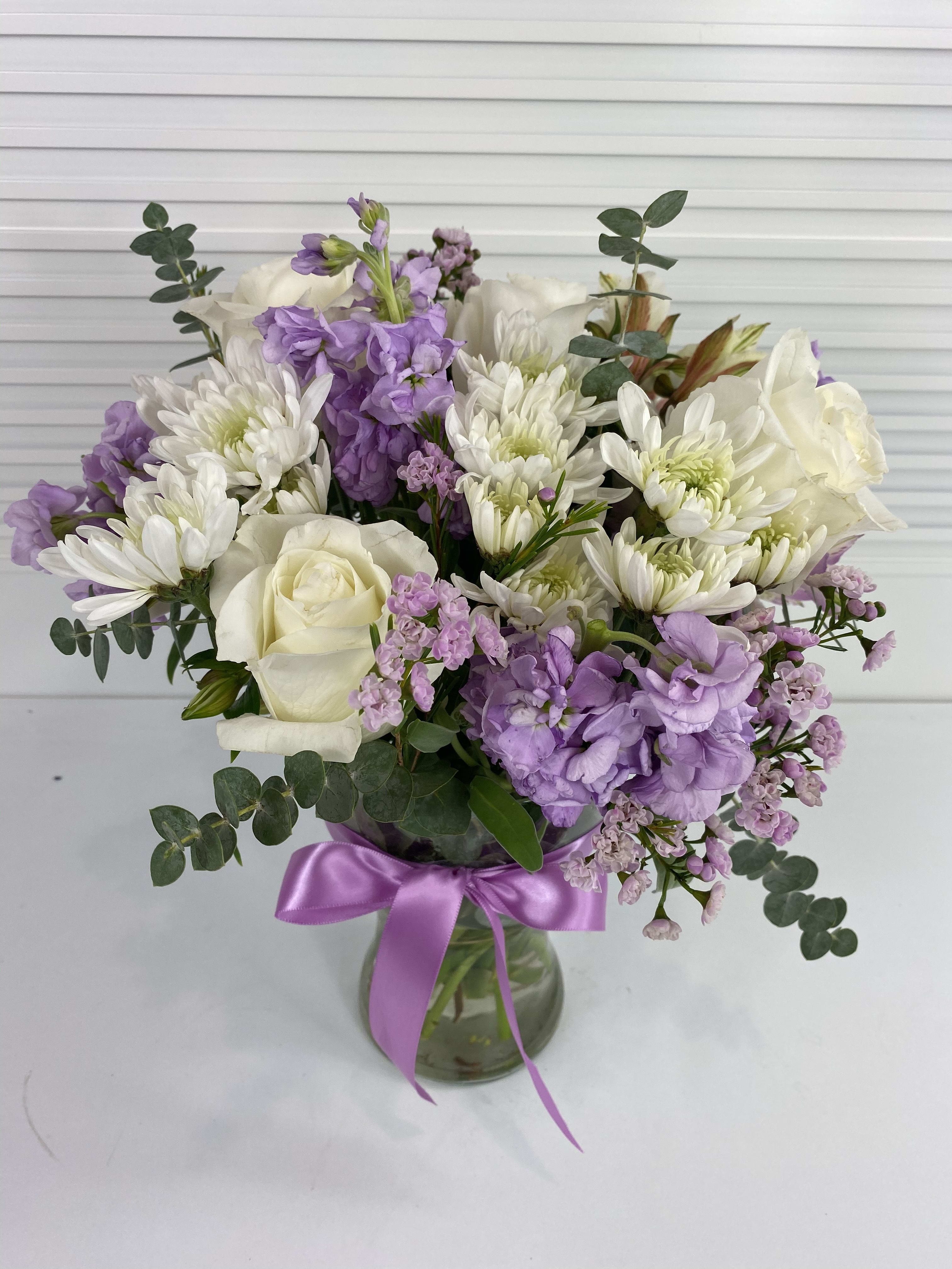 Soft Lilac - White roses, stocks, wax flower, daisies, alstroemerias and eucalyptus in a clear vase