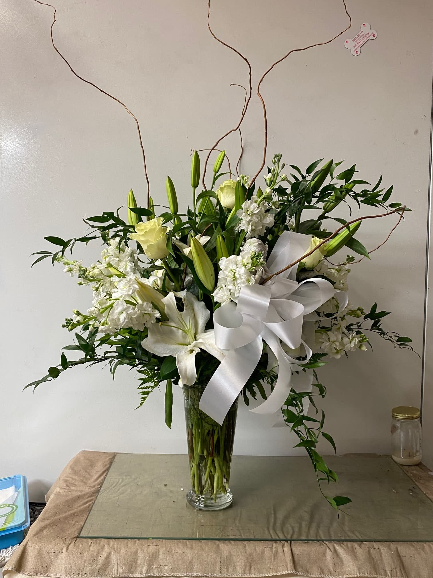 All white flowers - White roses, stock, snapdragons, curly willow and lilies with mixed greens.  A white bow was added.