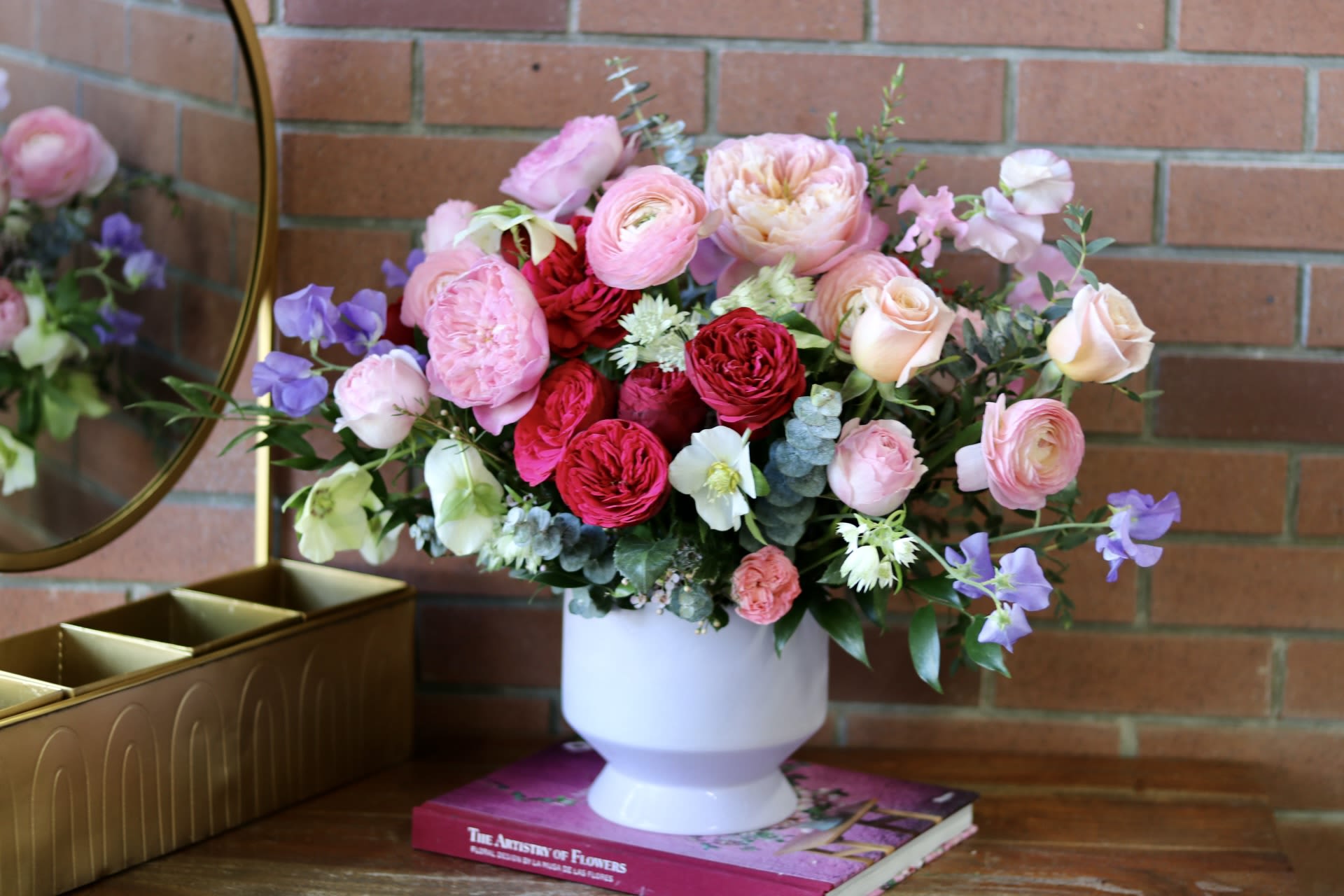 Love Poetry  - Let your love speak volumes this Valentine's Day with our enchanting 'Love Poetry' arrangement. Each bloom has been carefully chosen to tell a story of romance and devotion, featuring luxurious garden roses in passionate red and tender pink hues that unfold like verses of a love sonnet. Delicate sweet peas in soft lavender dance through the arrangement like whispered words, while pristine hellebores add their quiet grace.   The bouquet's gentle palette transitions from deep crimson to the softest blush, reminiscent of love's many expressions. Fresh eucalyptus and refined greenery weave throughout, creating natural rhythm and movement. Artfully arranged in our signature white vessel, this masterpiece stands as an eloquent declaration of affection.  'Love Poetry' captures the essence of romance - both bold and tender, classic yet fresh, making it the perfect Valentine's gesture for someone who appreciates the artistry of flowers and the language of love.