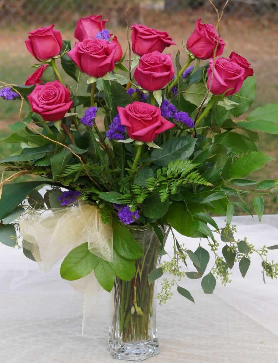 One Dozen Hot Pink Roses with Statice - Our One Dozen Hot Pink Roses with Statice is a bright and vibrant eye-catcher.  This dozen is artfully arranged in a heavy, clear, panel vase accompanied by seasonal mixed greens.  The purple statice is a modern touch that will make you look twice.  This modern beauty is appropriate for an anniversary, birthday or funeral.    APPROXIMATE DIMENSIONS - 24&quot; in  x 24&quot; in  