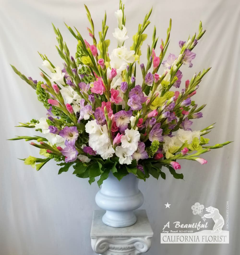 Sympathy in Pastel - Sympathy in Pastel is a stately, sophisticated tribute of white and soft pastel gladiolas beautifully arranged in a white urn vase. Accents of lush greens are added at the base and rear to finish this showy arrangement. Pastel colors of gladiolas will vary, based on seasonal availability, please call us direct to inquire for specific color. Approximate size is 34" tall by 34" wide. 