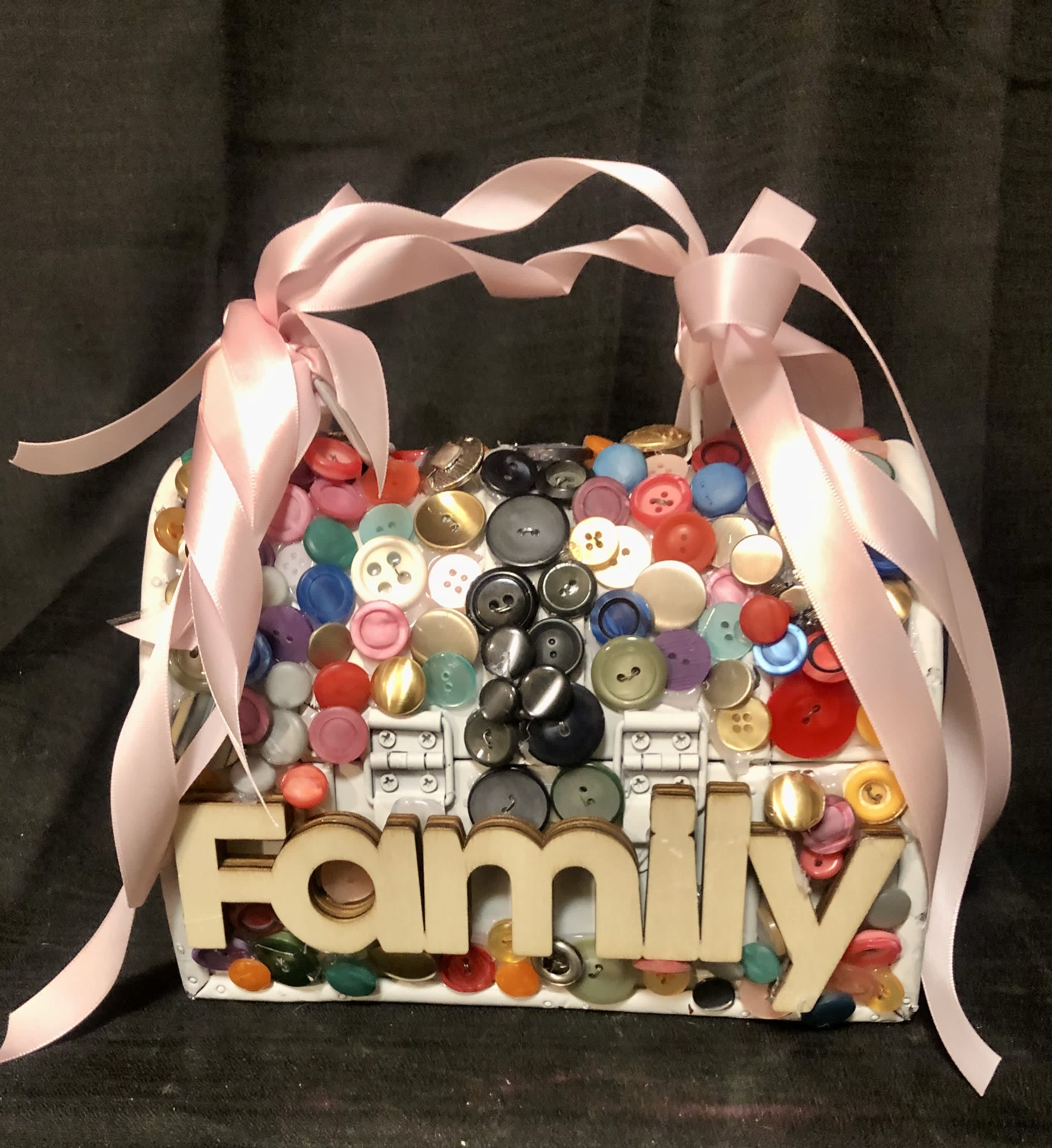 CUTE AS A BUTTON-BLOOMBOX - A small purse, embellished with assorted colored buttons, the word Mom and a rhinestone butterfly. The back has the the word family, toped off the a satin ribbon handle, filled with seasonal fresh blooms, to match.