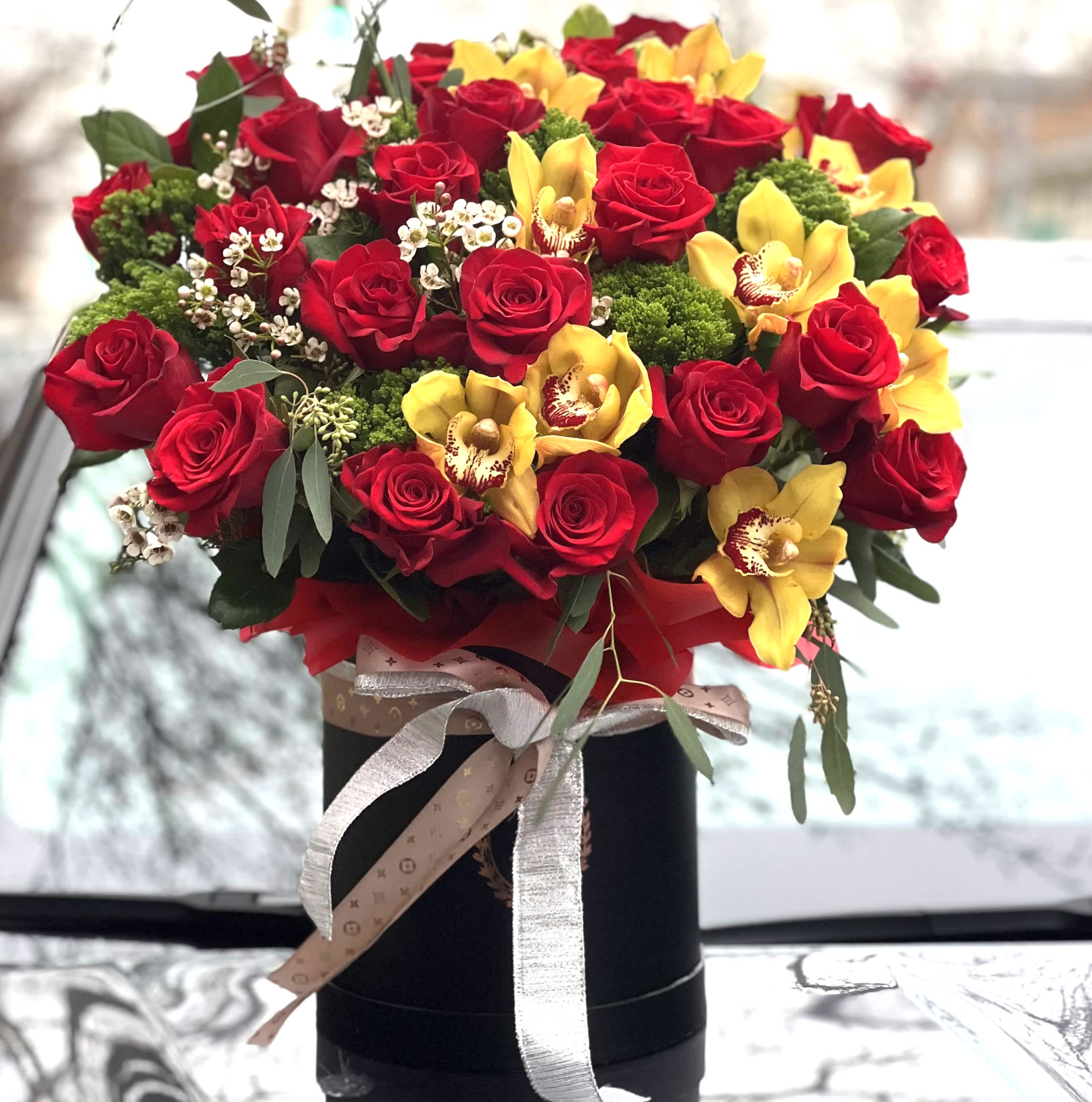 Scarlet Elegance Scarlet Elegance - An arrangement that captures the essence of opulent beauty. This stunning bouquet features a lavish mix of deep red roses and vivid yellow orchids, each flower selected for its perfection and vibrancy. The roses symbolize a love that is both passionate and enduring, while the orchids bring a touch of exotic sophistication, creating a harmonious blend of color and texture. Accented with delicate white blooms and lush greenery, the bouquet is presented in a sleek black vase, tied with a designer ribbon that adds a touch of luxury. "Scarlet Elegance" is a celebration of love's rich tapestry, perfect for those moments when only the most exquisite gesture will do.