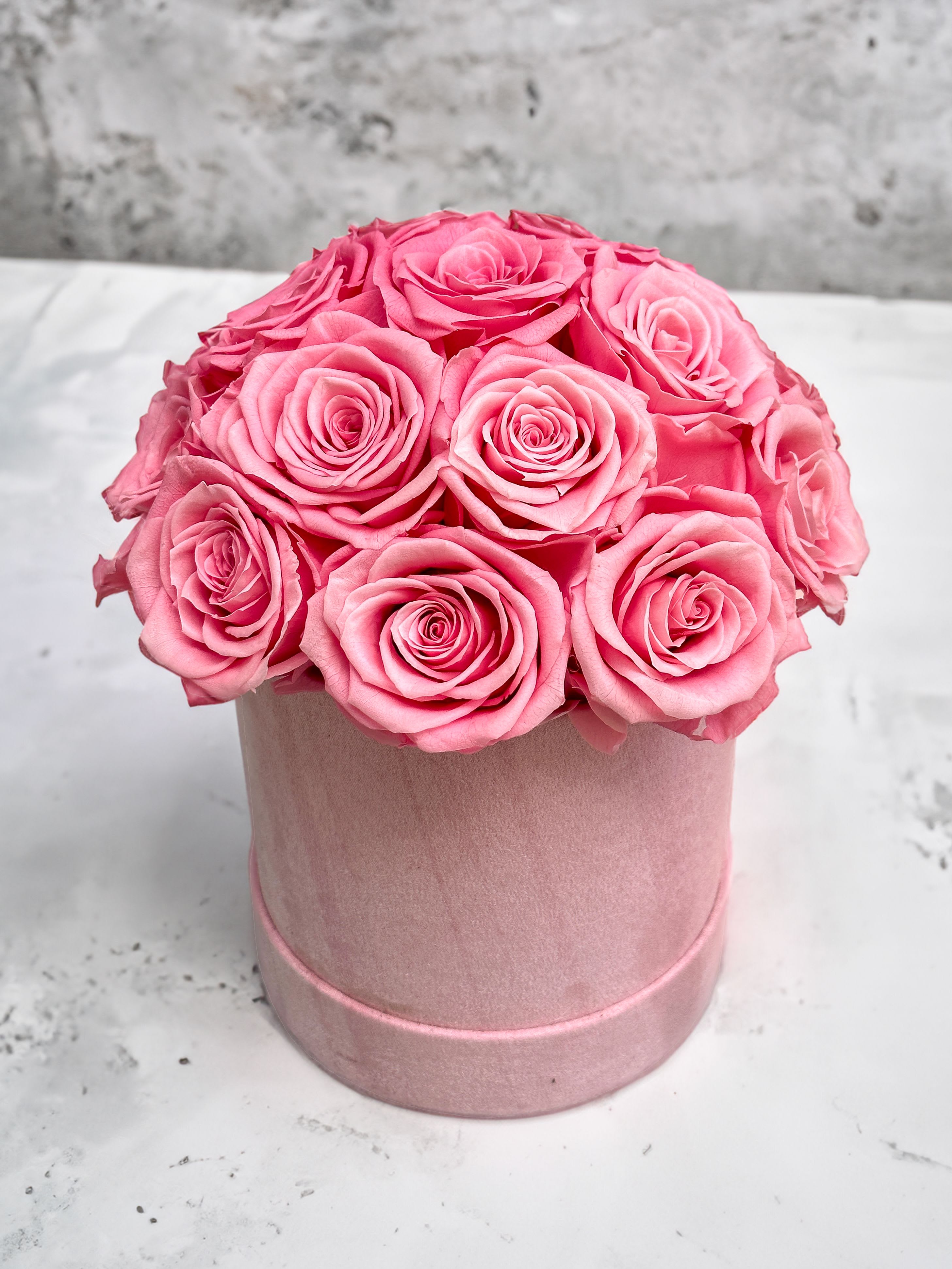 Forever Roses - Pink - Elevate your space with our luxurious velvet cylinder box featuring real preserved roses. Available in arrangements of 16, 25, or 30 roses, each box showcases a dome-shaped arrangement of exquisite Ecuadorian preserved roses in your choice of red, white, light pink, or hot pink. Nestled within a plush velvet cylinder box, this stunning bouquet offers timeless beauty and elegance that lasts for years.  Our Forever Roses are the perfect way to show your love and appreciation - forever. Our exquisite roses are preserved to maintain their delicate beauty, for a sophisticated gift that will last a lifetime. Each rose dome is presented in an elegant velvet gift box, offering a truly special token of your affections.  Perfect for any occasion or as a striking decor piece, these preserved roses provide a maintenance-free alternative to fresh flowers, requiring no watering or upkeep. Each rose is carefully preserved to maintain its vibrant color and delicate texture, ensuring a long-lasting display that adds a touch of sophistication to any setting.  Standard : 16 Roses Deluxe: 25 Roses Premium: 30 Roses  Product Features:  • Luxurious Arrangement: Choose from 16, 25, or 30 preserved roses arranged in a dome shape. • Elegant Color Options: Available in red, white, light pink, or hot pink. • Velvet Cylinder Box: Packaged in a plush velvet box for a touch of luxury. • Maintenance-Free: No watering or wilting, offering enduring charm.  Box Dimensions:12x10x10 