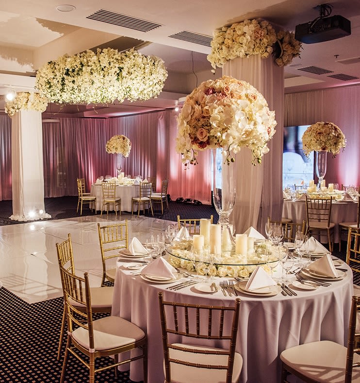 Wedding Designs Los Angeles - Celebrate your love story with a wedding design that radiates elegance and charm. Our premium wedding decor services in Los Angeles are tailored to create a captivating atmosphere for your special day. This setup showcases tall floral centerpieces in soft pastel tones, paired with luxurious gold accents and a warm glow from candlelight, offering a perfect balance of sophistication and romance.  From intricately designed ceiling installations to elegantly draped fabric that enhances the venue’s ambiance, every element is thoughtfully curated to reflect your style. Our approach focuses on seamless harmony between floral artistry, lighting, and decor, ensuring a memorable experience for you and your guests. Whether you desire a classic look or a modern aesthetic, we work closely with you to bring your dream wedding to life.  Trust our team to deliver a flawless event with unmatched attention to detail and passion for creating stunning celebrations. With years of expertise in wedding decor, we specialize in transforming ordinary spaces into extraordinary settings, filled with beauty and love.