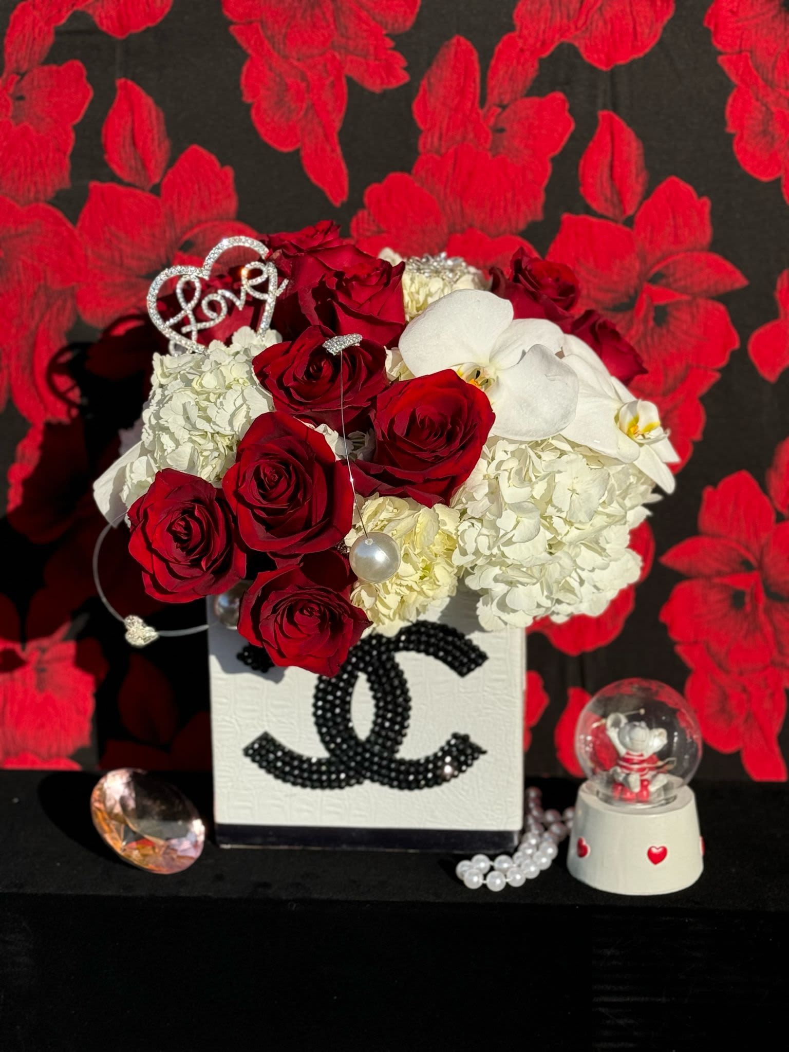 Elegance in White: Designer Box Floral Arrangement with Accessories - Experience the epitome of sophistication with this exquisite floral arrangement presented in a sleek, high-quality white designer box. The arrangement features a curated selection of premium blooms—such as elegant roses, hydrangeas and delicate orchids—artfully arranged to create a harmonious and graceful display. To enhance the beauty and thoughtfulness of the gift, the box is paired with luxurious accessories. 