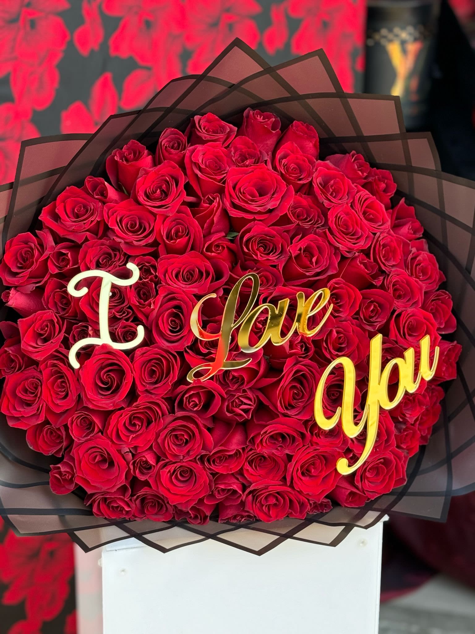 100 Red Roses: A Grand Declaration of Love - Express your deepest emotions with a breathtaking arrangement of 100 vibrant red roses, symbolizing pure love and affection. Each rose is hand-selected for its beauty and freshness, carefully arranged to create a stunning display that speaks volumes. This magnificent bouquet is a powerful way to say &quot;I love you&quot; with designer paper or just in black, the gold acrylic sign makes it the perfect gift for a romantic gesture or a significant moment in your relationship. The overwhelming beauty and meaning behind 100 red roses will leave an unforgettable impression, conveying your love in the most grand and heartfelt way.