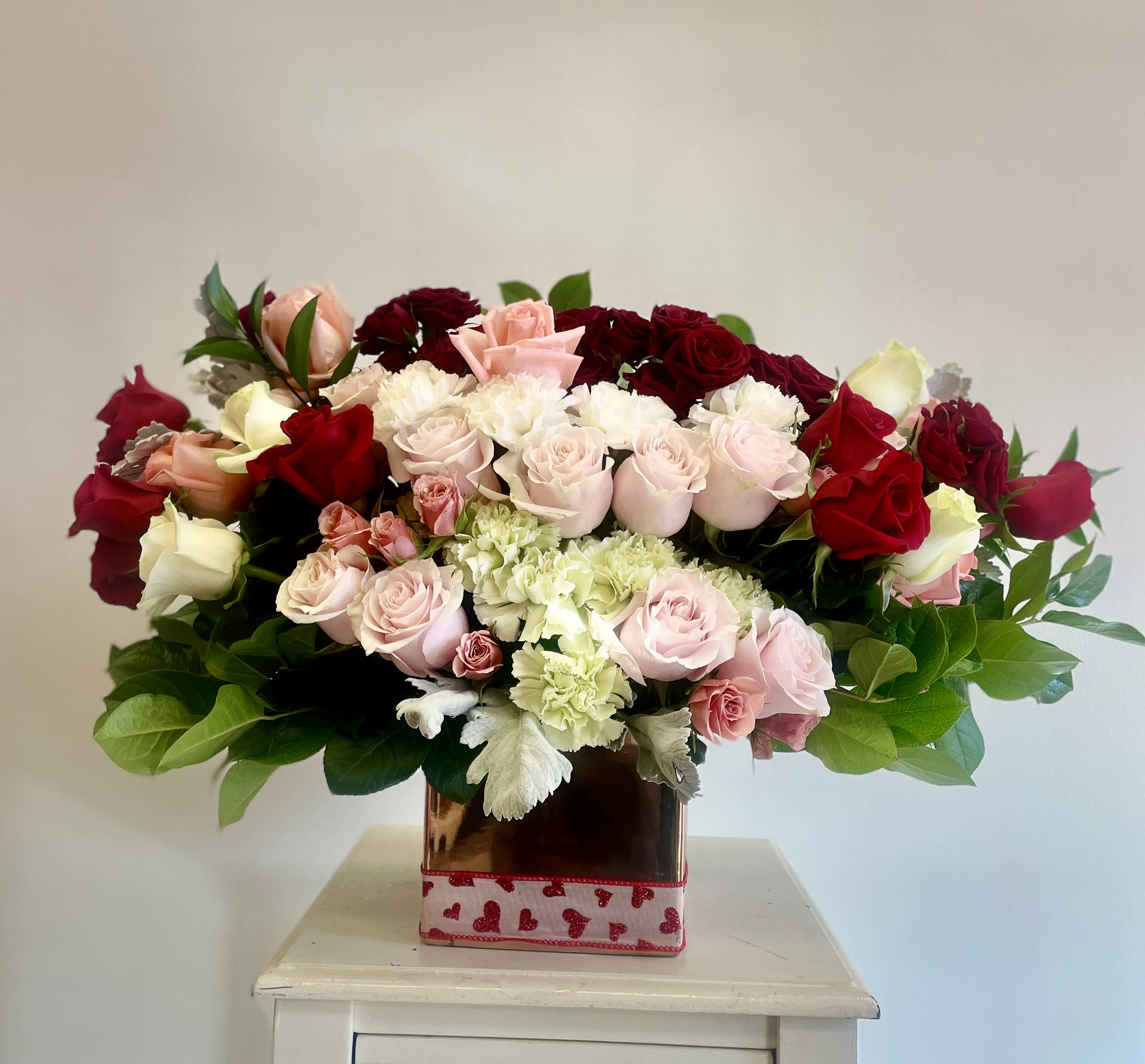 Angella Bella - Majestuoso Arreglo de 24 rosas en forma ovalada con 12 Carnation, Salal, Ruscus , Spray roses y Dustin Miller. El arreglo mide 2 pies.