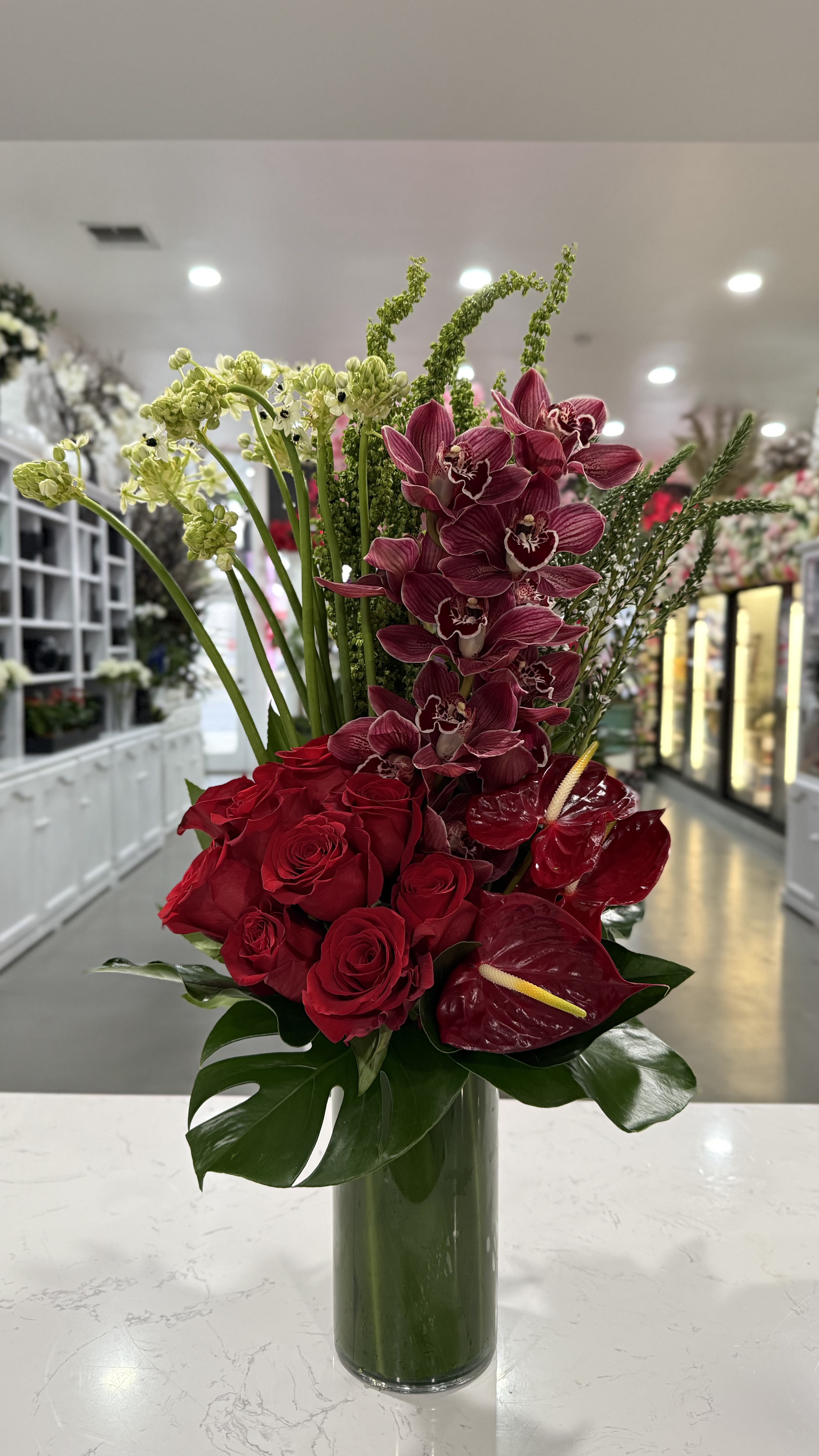 Modern Love - A sleek and passionate arrangement of rich red roses, exotic burgundy orchids, and striking anthuriums, accented with lush greenery for a contemporary and romantic look.