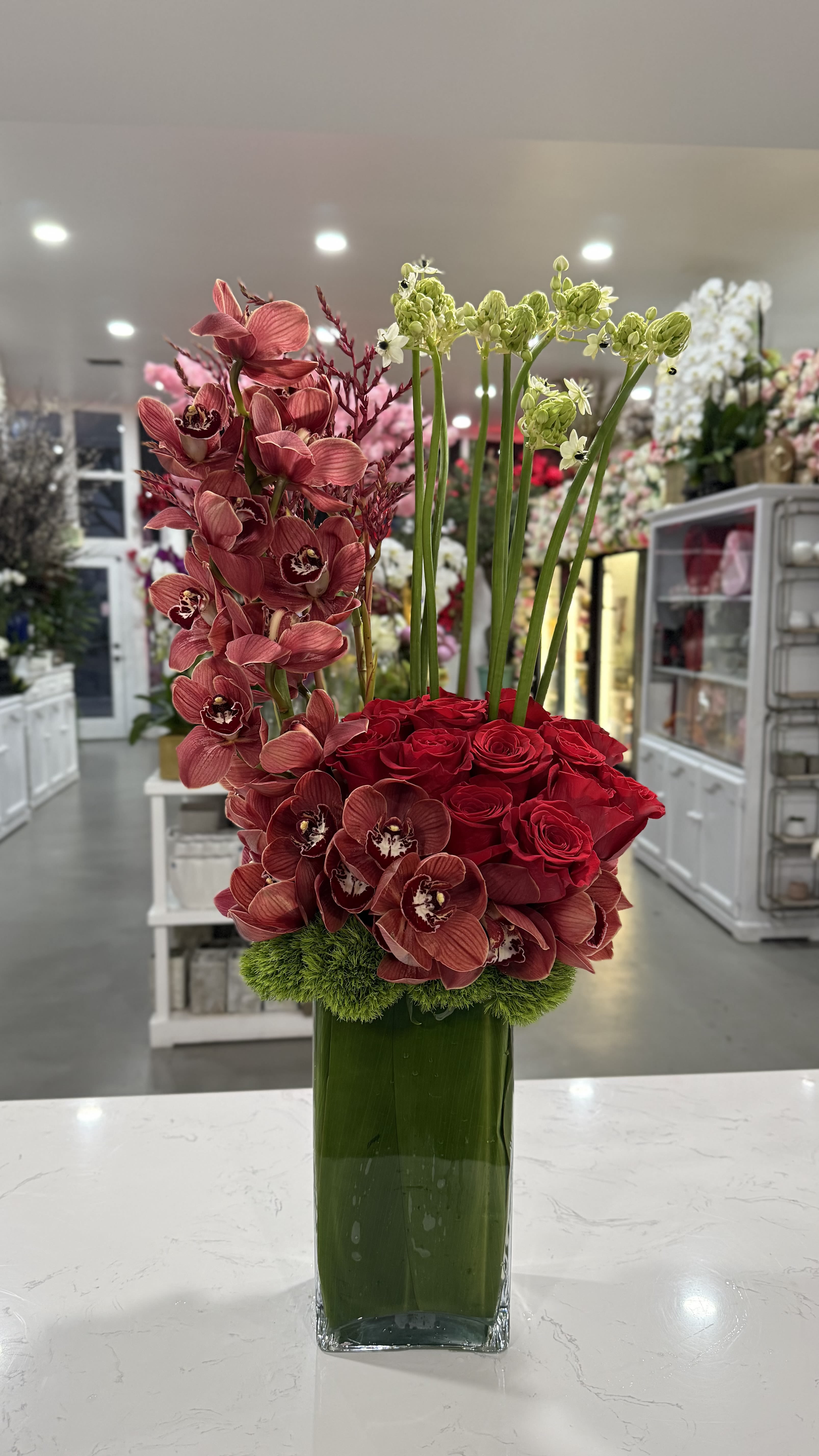 Rouge Vibe - A sleek and modern blend of rich red orchids and roses, accented with fresh green textures. Designed for those who love bold, sophisticated, and contemporary floral aesthetics.