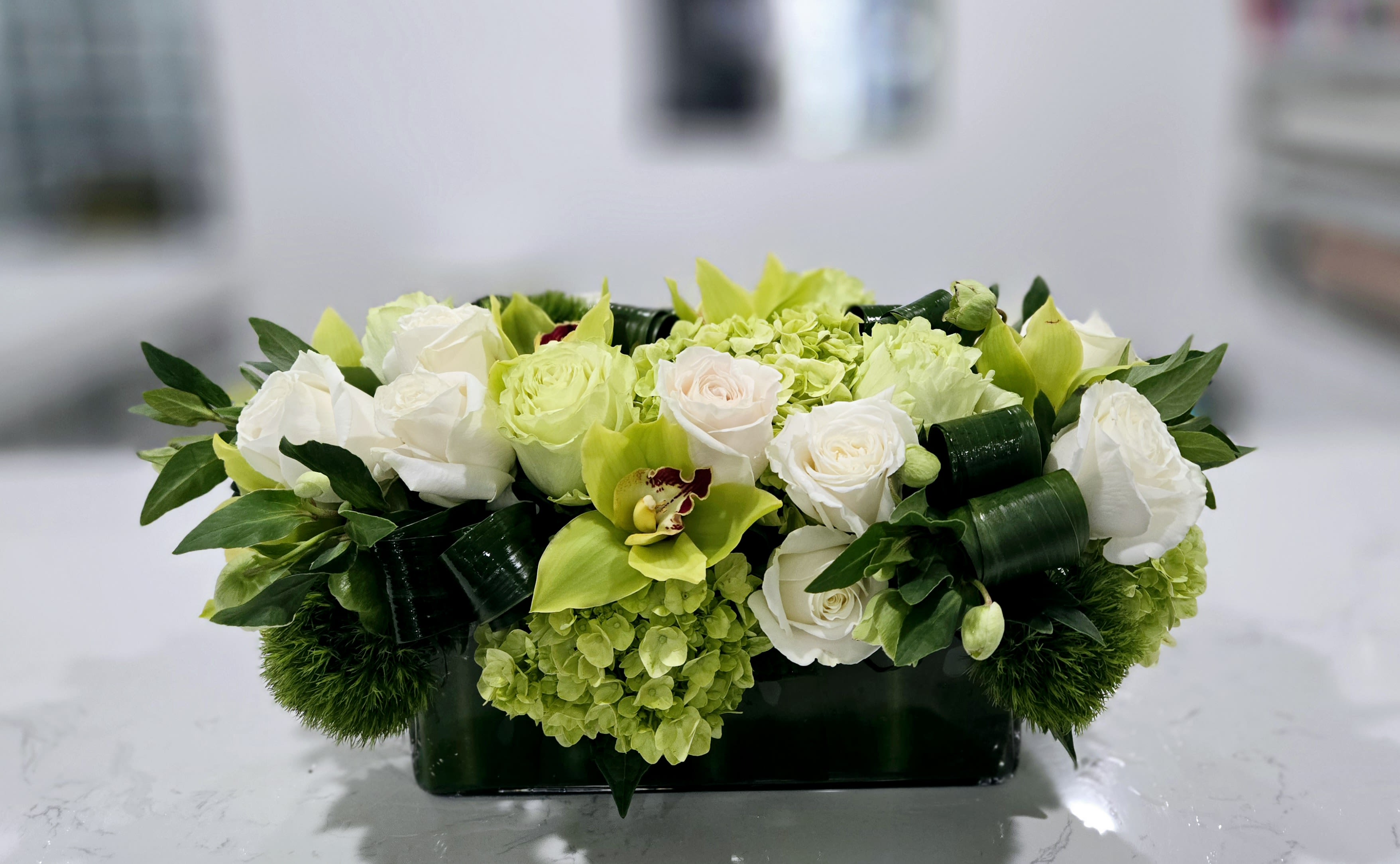 Green Luxe - A fresh, modern blend of white roses, lime green hydrangeas, and vibrant green orchids, accented with lush greenery. This sleek design brings a clean, elegant touch to any setting, perfect for contemporary spaces.