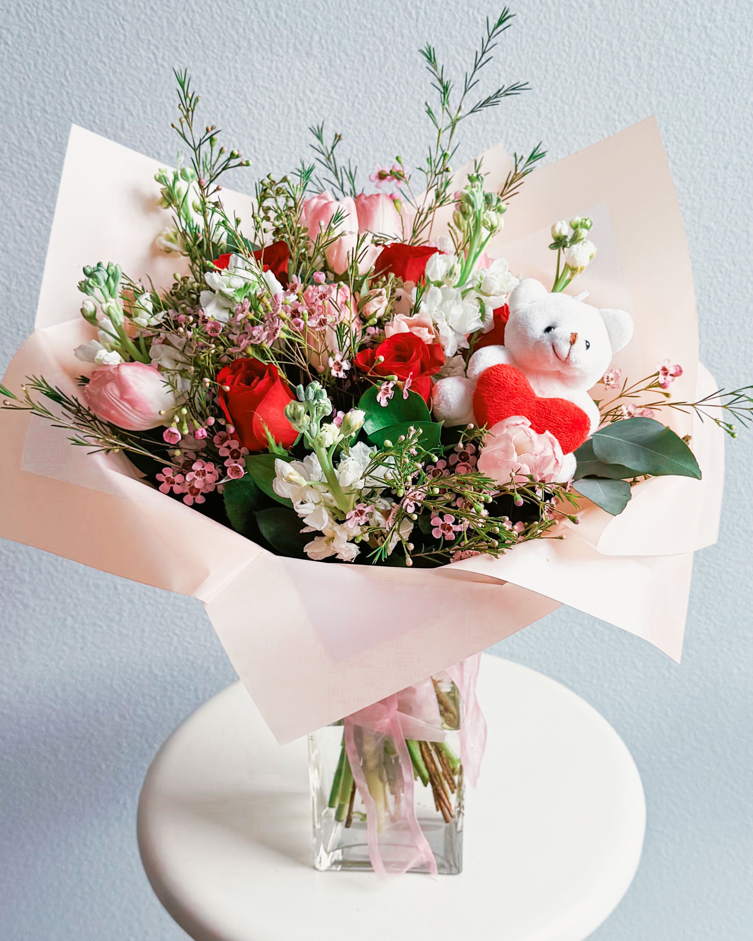 Teddy Touch - This bouquet is pure sweetness! A dreamy mix of red and blush roses, soft pink tulips, and delicate white stock, all wrapped up with a lil’ teddy for extra cuteness. The fresh waxflowers and eucalyptus add that soft, romantic touch, while the teddy bear makes sure your message is extra cozy. Perfect for Valentine’s Day, anniversaries, or just because you wanna make someone smile!