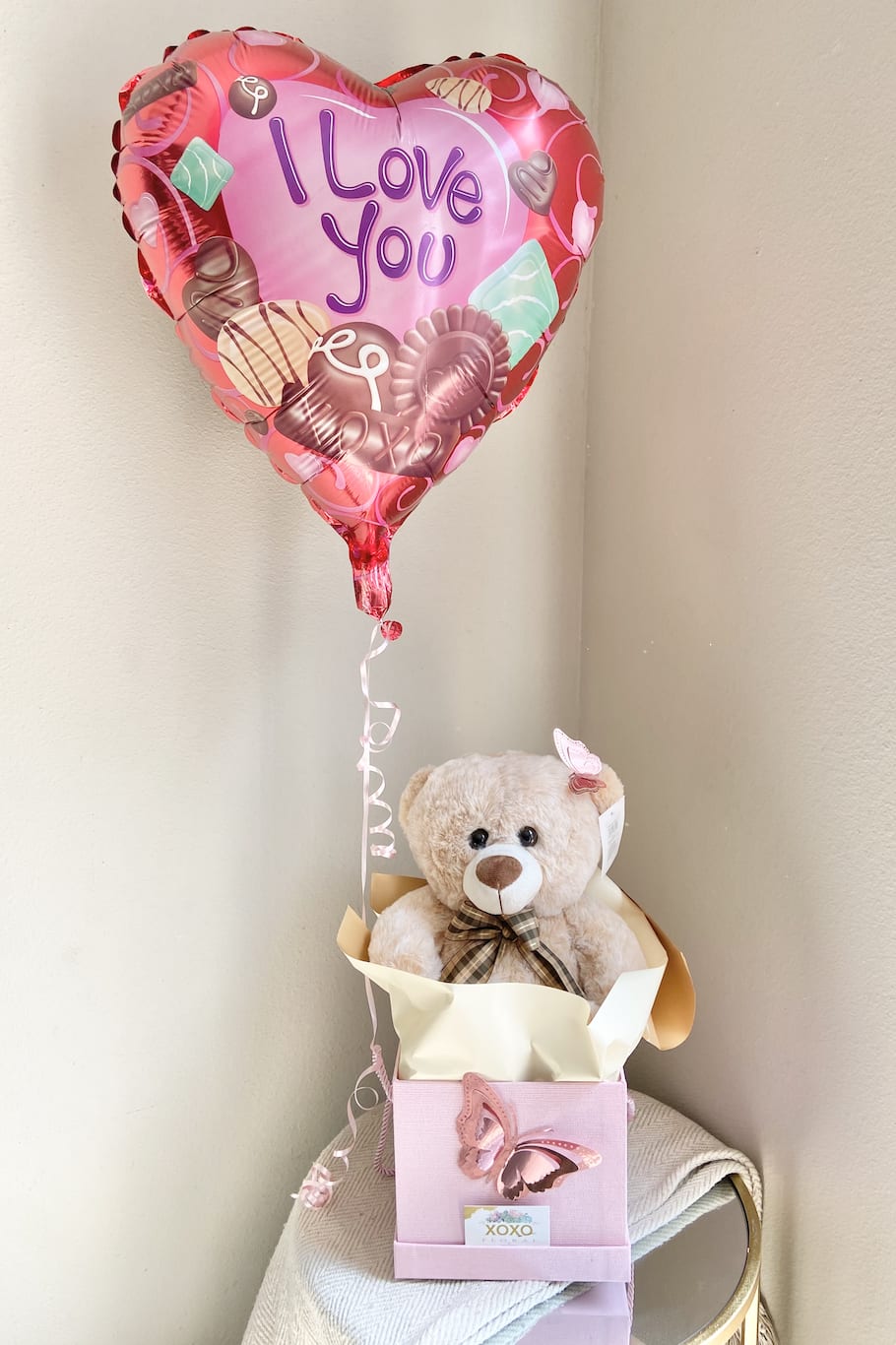 Teddy Bear with Balloon - Teddy bear and balloon gift box This is a soft, cuddly teddy bear nestled inside a charming gift box, its plush fur in a warm, honey brown hue. The bear’s stitched smile and button eyes exude warmth and friendliness, as if it’s waiting for a hug. Its little arms are open, inviting you to embrace it, while its tiny nose adds a sweet, endearing touch.  The bear is cradled gently in a box lined with soft tissue paper, which adds an extra layer of coziness and surprise. Above the bear, a mylar helium balloon floats gracefully, its vibrant color contrasting against the neutral tones of the bear. The balloon can be tailored to fit the occasion perfectly, adding a personal touch to the gift. Here are some ideas for different occasions -I love you -happy birthday -Just because -Smiley face The entire presentation is both playful and heartwarming, creating a gift that's not only adorable but also full of thoughtfulness and charm. It’s a perfect gift for someone who could use a little extra comfort or joy.  Text us the occasion for your balloon (714)360-5020