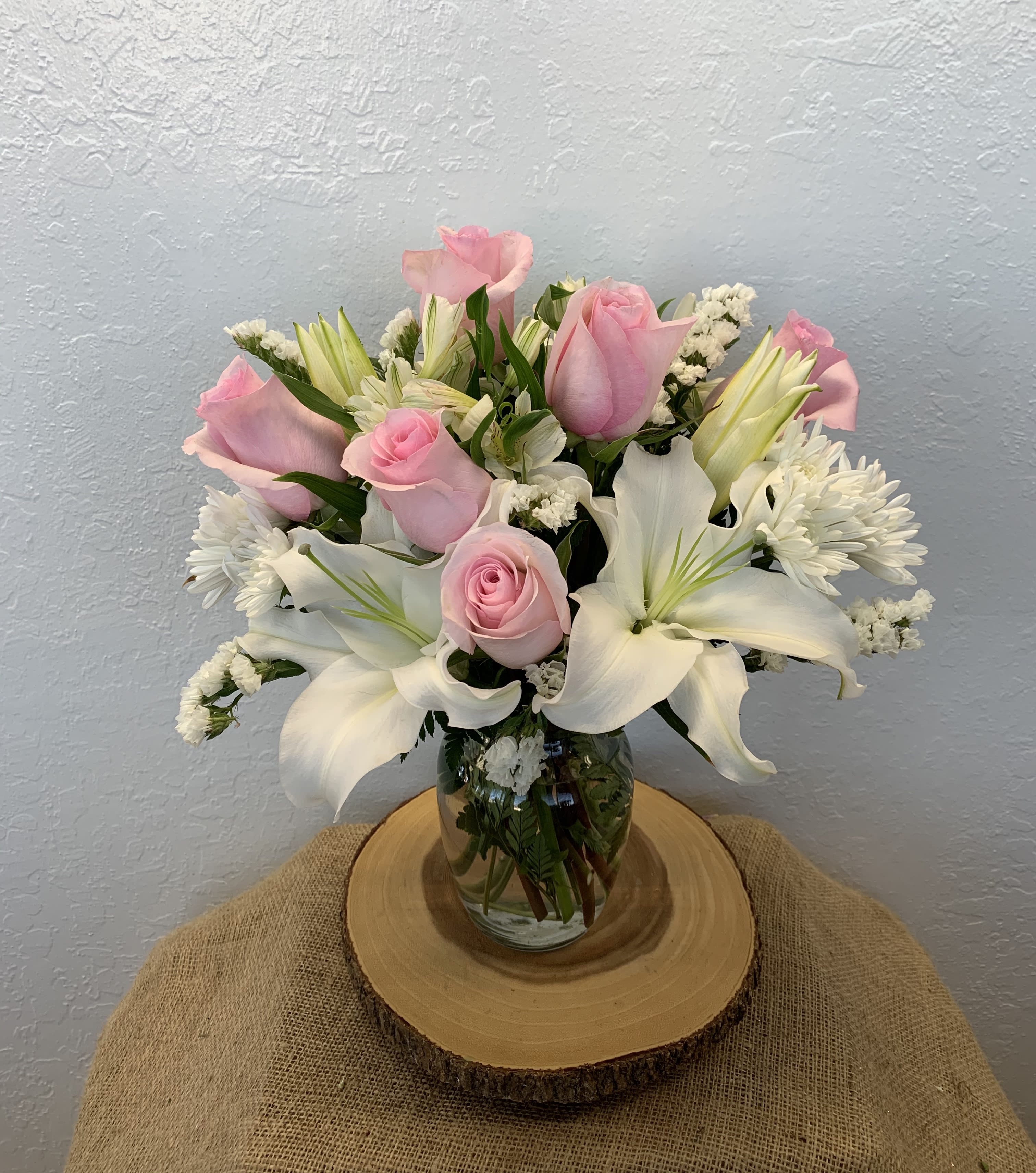Lady of Bliss - The stems of beauty and grace... this alluring bouquet will be sure to lure you in. This arrangement features pink roses, lilies, alstroemerias, cushion poms, statice, and mixed foliage in a glass vase.