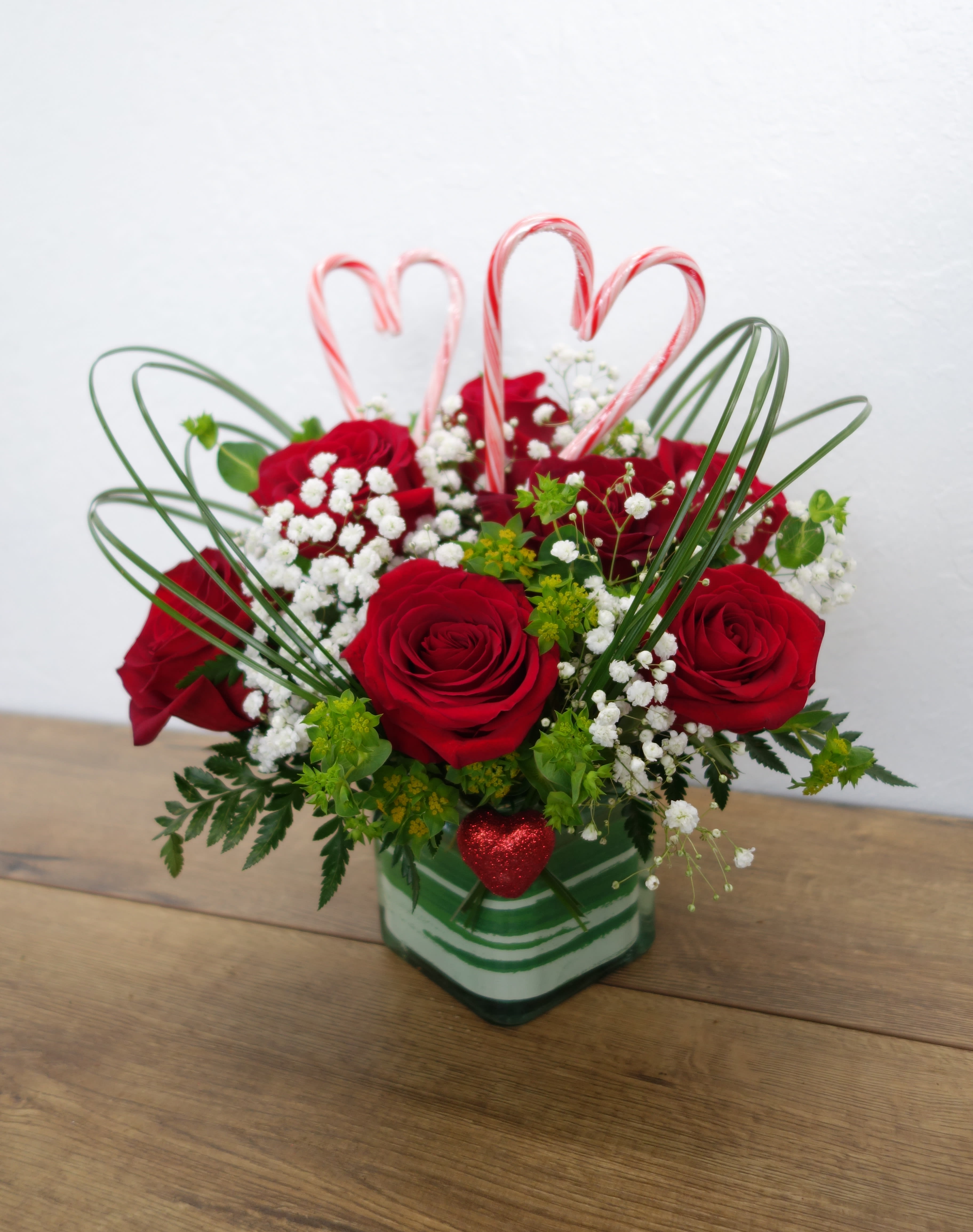 Heartstrings - One look and this bouquet will tug on their heartstrings! This lovely arrangement features 7 roses, baby's breath, and mixed foliage, accented by beargrass and a pair of candy cane hearts in a glass cube vase.  Standard (as shown): 7 roses Deluxe: 9 roses Premium: 11 roses  Measurements: Approx. 11&quot; x 11&quot;