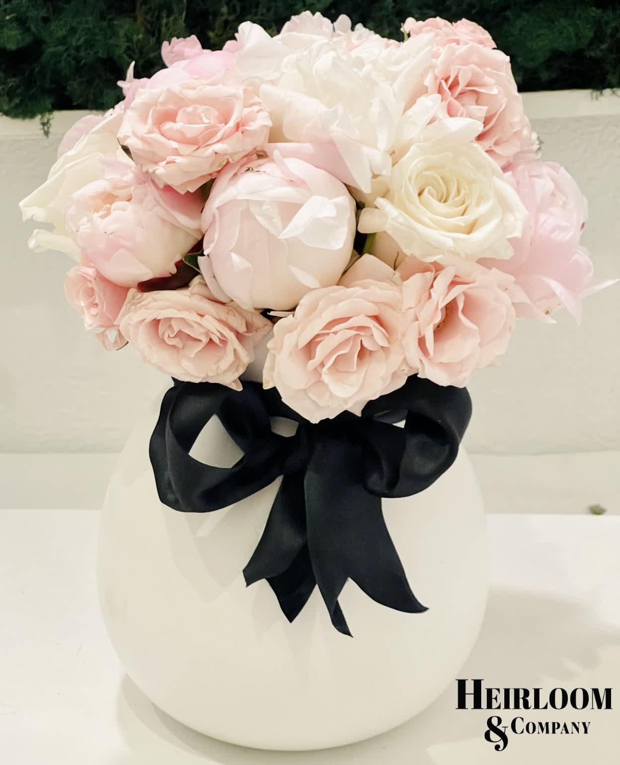 Peonies and Champagne Peonies and Champagne - A white ceramic vase filled with fresh handpicked Pennie’s, roses, and mini spray roses in a blush and white palette, wrapped together with a satin black bow