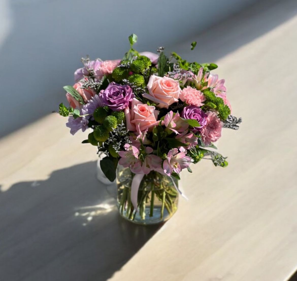 Garden Vibes  - This is a perfect arrangement with the perfect variety of flowers! Includes purple rose, pink rose, pink alstroemeria, green button Pom poms, pink carnation, misty blue, lavender Pom poms, greenery in a clear vase. 