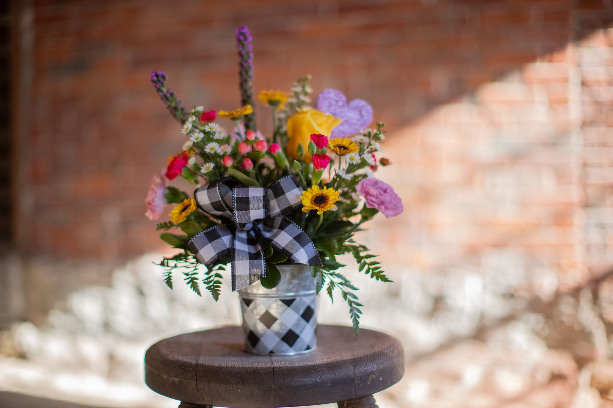 Just Friends  - Looking to send something special this Valentines Day? This fun and colorful design is the perfect way to show a friend or family member some extra love this season. This design features a variety of spring blooms paired with a plaid tin container and bow. Featuring a single yellow rose and glittering heart pick, this design by Katie is sure to make any recipients heart sing. Premium upgrade includes larger container.