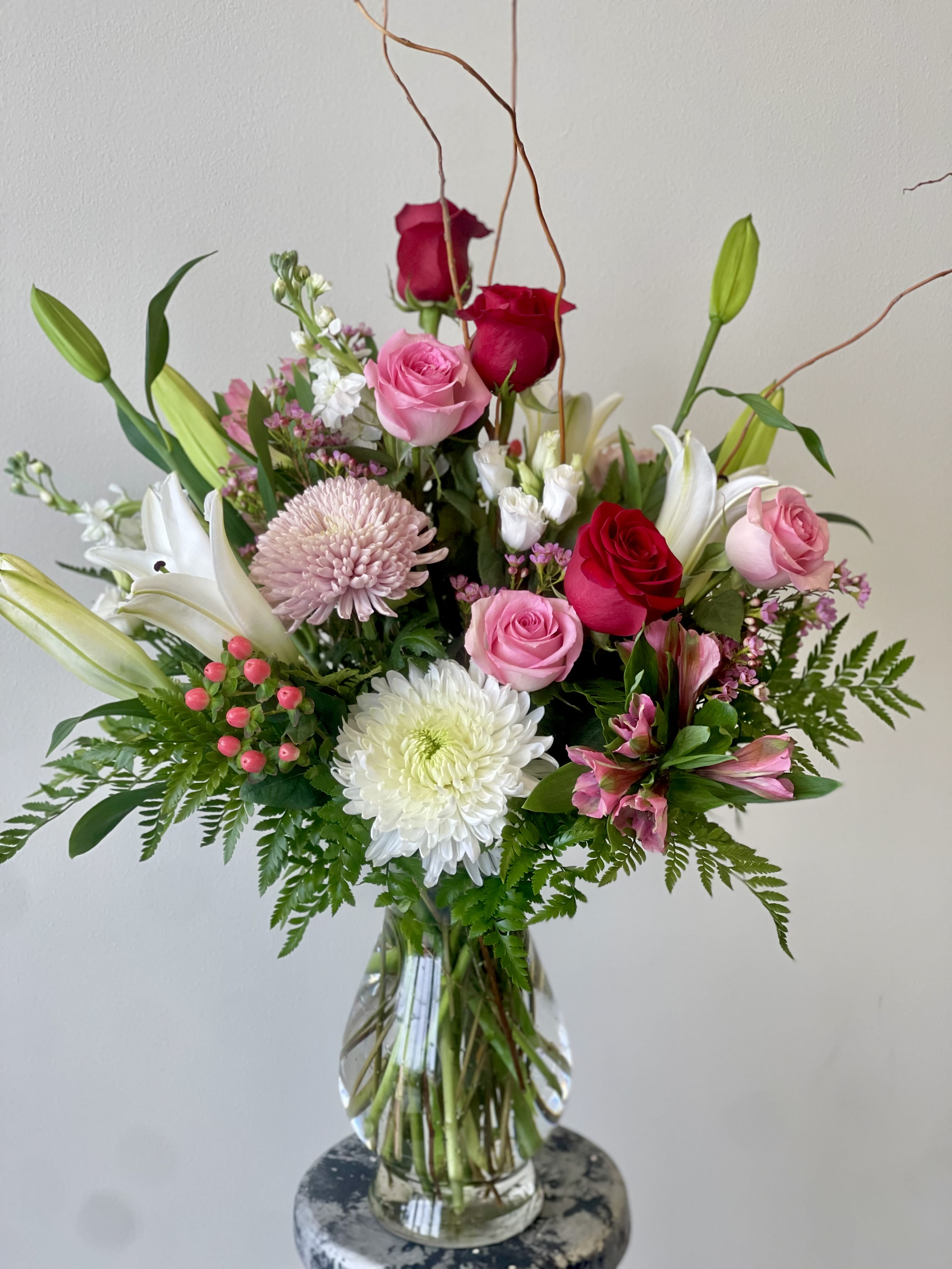 Cupids Love  - A pink, red, and white Valentine's Day floral arrangement typically features a beautiful mix of roses, peonies, and lilies. The soft, romantic pinks evoke love and affection, while the deep reds symbolize passion and desire. White flowers, like lilies or daisies, add purity and elegance to the bouquet. Greenery and delicate filler flowers, like baby’s breath, are often included to enhance the arrangement and give it a fresh, full look. The combination of these colors creates a balanced, stunning display perfect for celebrating love and affection on Valentine’s Day. It’s a timeless and classic choice for expressing deep emotions.