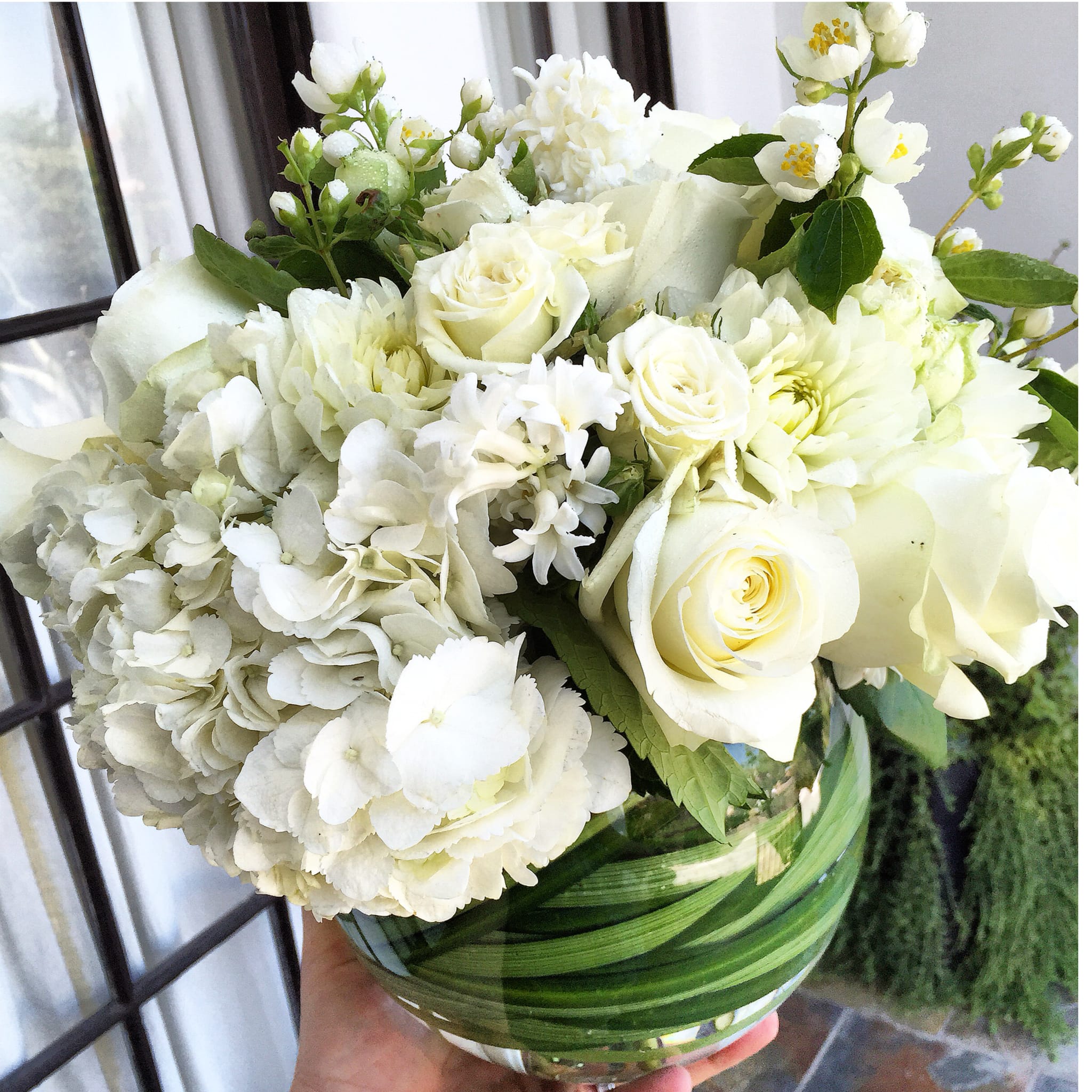 The Lady in White Arrangement. - This Darling beaming in her Summer Whites, Delicious Proud Roses, Potent Sweet Hyacinth, Feisty Dahlia, Bold Dutch Hydrangea, Sassy Spray Roses and a touch of Creamy Green Garden Spray Roses all bundled in a Glass Vase wrapped with Vibrant Green Lily Grass or Tea Leaves.