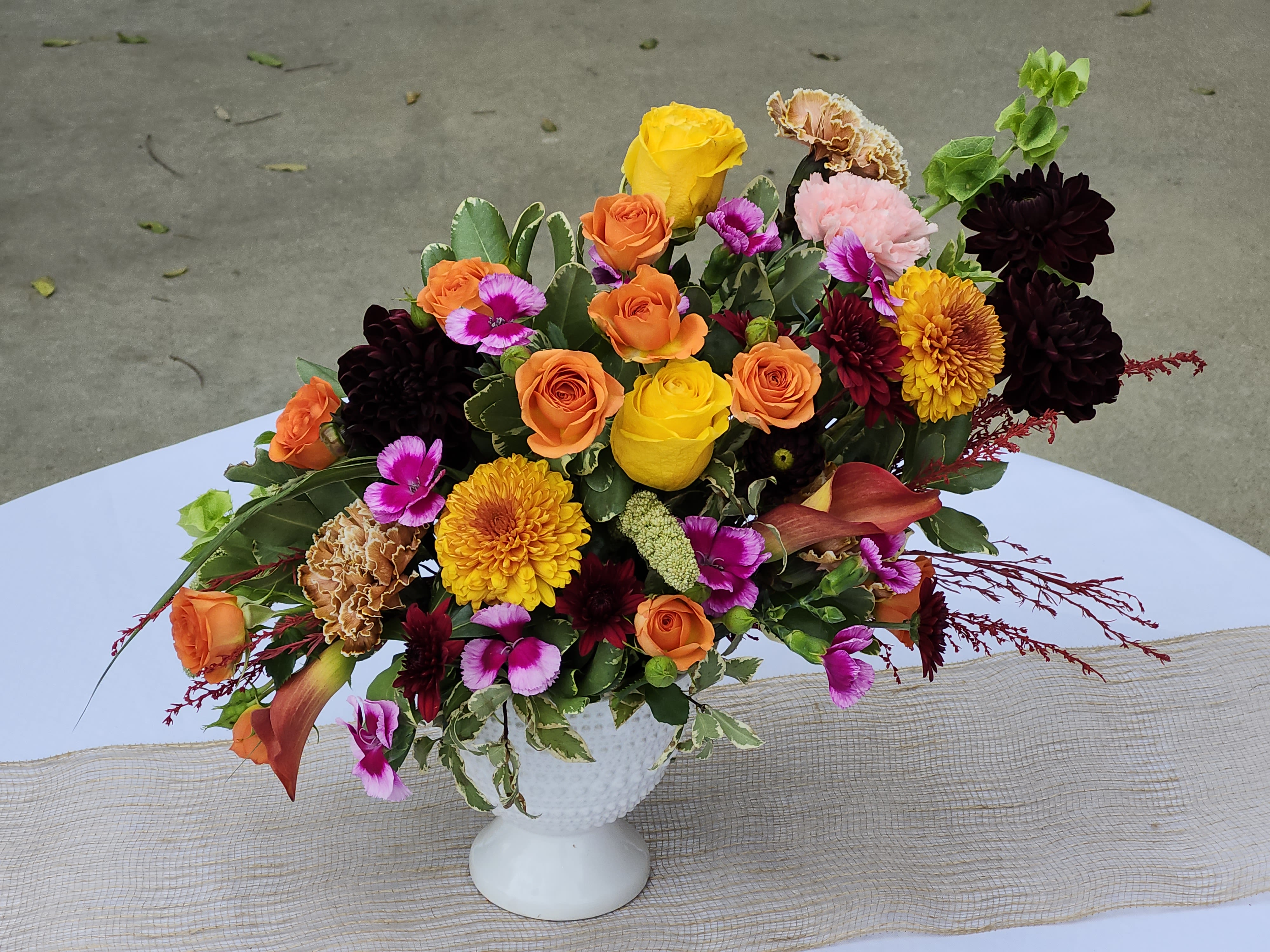 Lily Sunset - Fall elegant pedestal vase. Beautiful fall colors one sided V shape style. Great for desk or lobby counter. Flowers may vary during the season. Lillie's, carnations, roses, mums, dahlias, dianthis. Substitute may vary. 