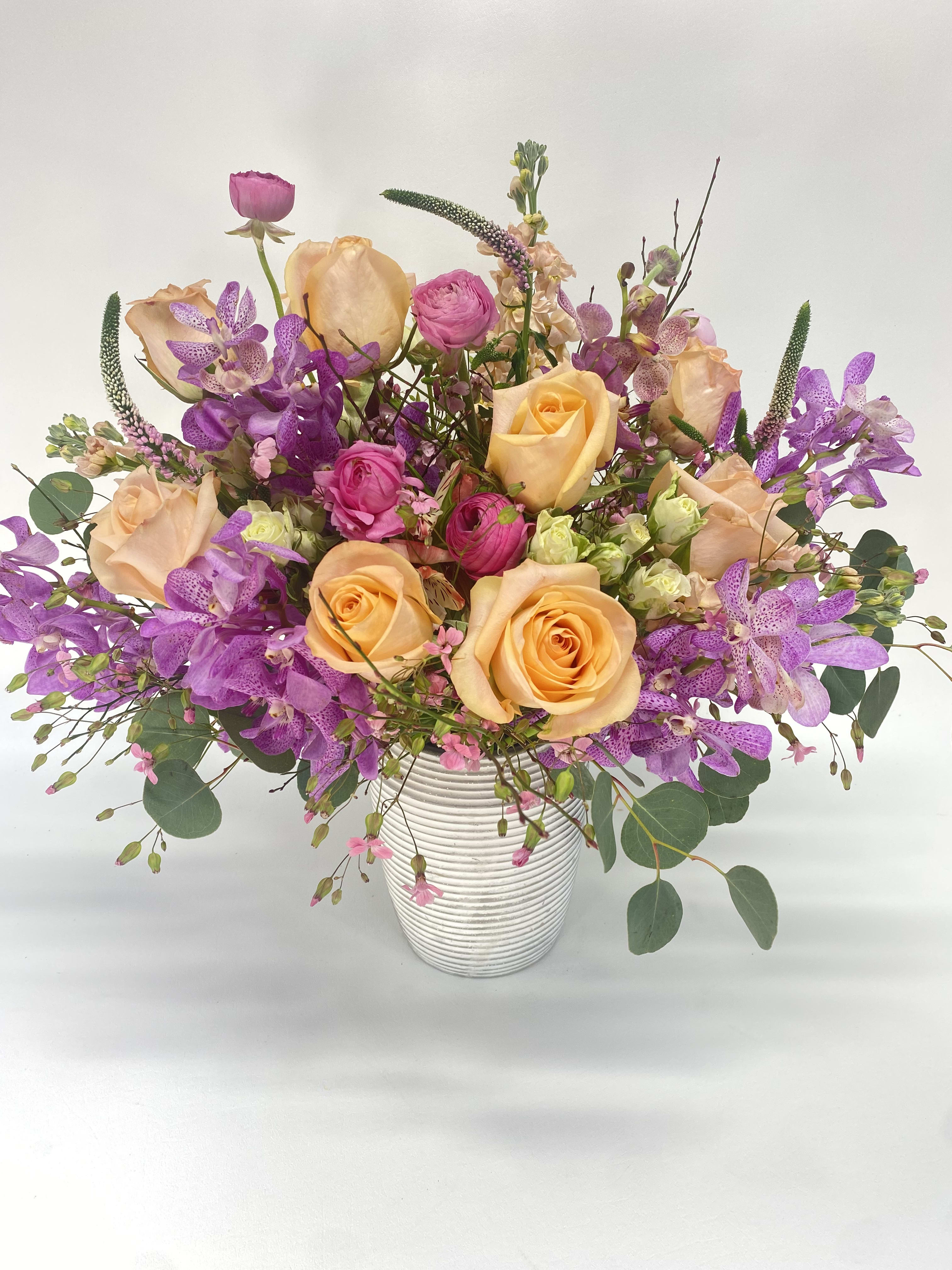 The Malibu The Malibu - Exotic soft purple orchids, peach Tiffany roses, Veronica, ranunculus, alstroemerias and fluffy fillers in a whitewashed ceramic vase.