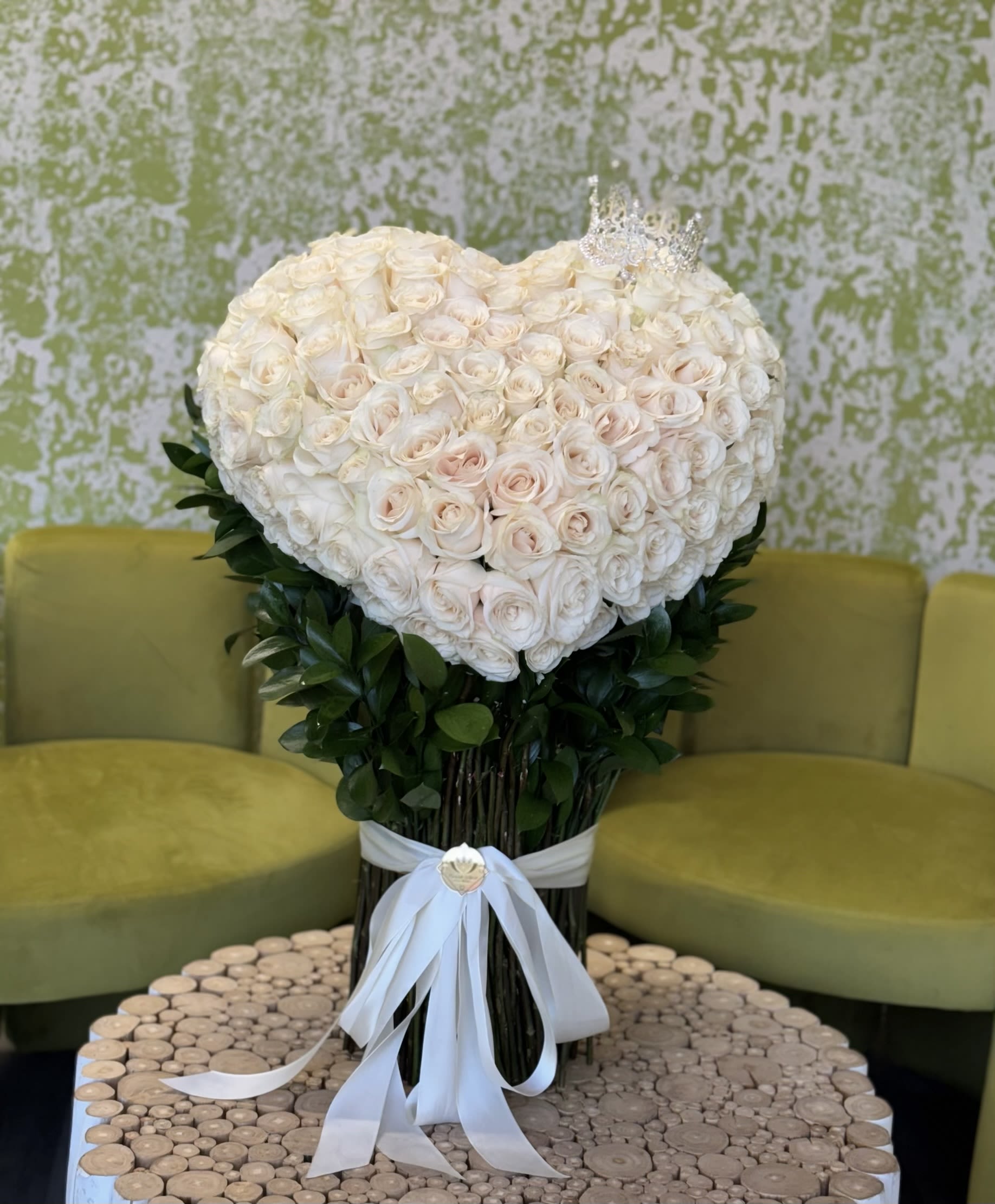 Regal Heart – Crowned Rose Masterpiece - Make a grand statement with our Regal Heart bouquet, a magnificent heart-shaped arrangement of premium white roses adorned with an elegant crown. This massive and luxurious design is perfect for showing your loved ones just how much they mean to you. With its stunning size and intricate details, this bouquet is truly a symbol of royalty, love, and devotion.  We can craft the same breathtaking arrangement with red or pink roses to match your loved one’s preference. Simply give us a call to check availability and create a personalized masterpiece. Perfect for Anniversaries, Proposals, Valentine’s Day, Weddings, Special celebrations of love.  