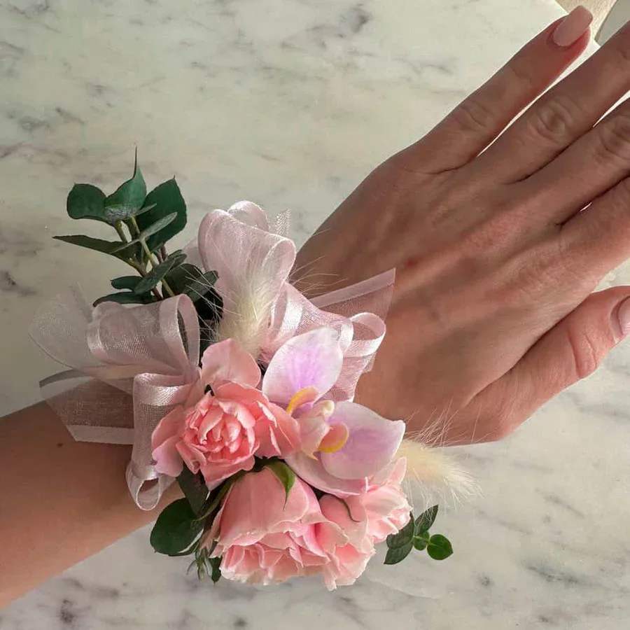 Pink Corsage - The enchanting Pretty in Pink Corsage, features a delicate mix of pink and peach roses, complemented by lush greenery. The pink roses symbolize gratitude and happiness, while the peach roses add sincerity and warmth. Perfect for weddings, proms, formal events, or celebrating special moments, the Pretty in Pink Corsage adds a touch of natural beauty to any occasion.