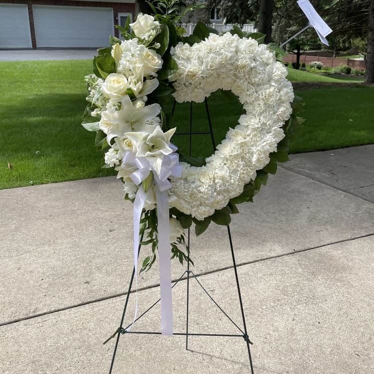 White Mix Heart Wreath White Mix Heart Wreath - Express your deepest sympathy with our White Mix Heart Wreath. This heart-shaped wreath, adorned with delicate dianthus, elegant roses, and serene lilies, serves as a heartfelt tribute to your loved one. Offering comfort and solace, this beautifully crafted arrangement is perfect for moments of remembrance and reflection.