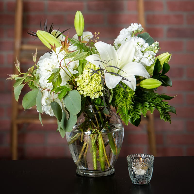 Garden Green (and white!) Garden Green (and white!) - a simple clear ginger vase is filled with foliages, hydrangeas and lilies, to showcase this low compact design style.
