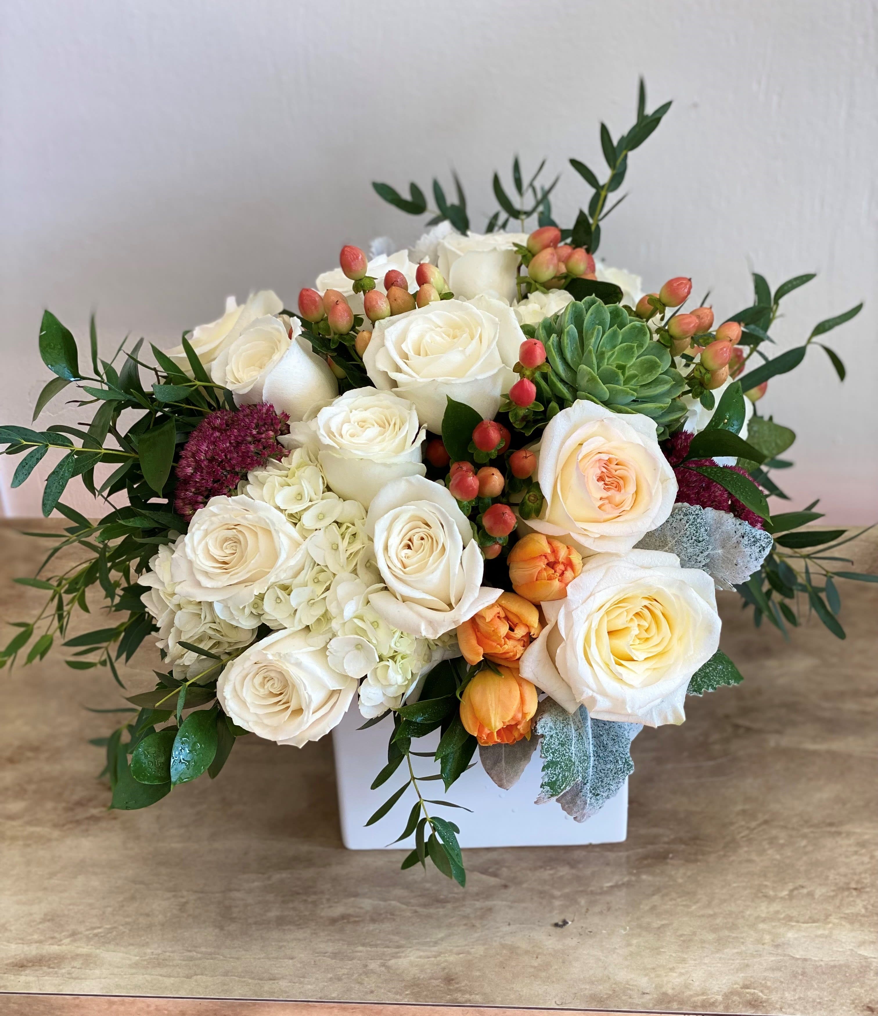 SOFT SENTIMENTS - A soft colored variety of beautiful flowers brought together in a white ceramic vase featuring roses, hypercium, succulents, and a variety of eucalyptus foliage.