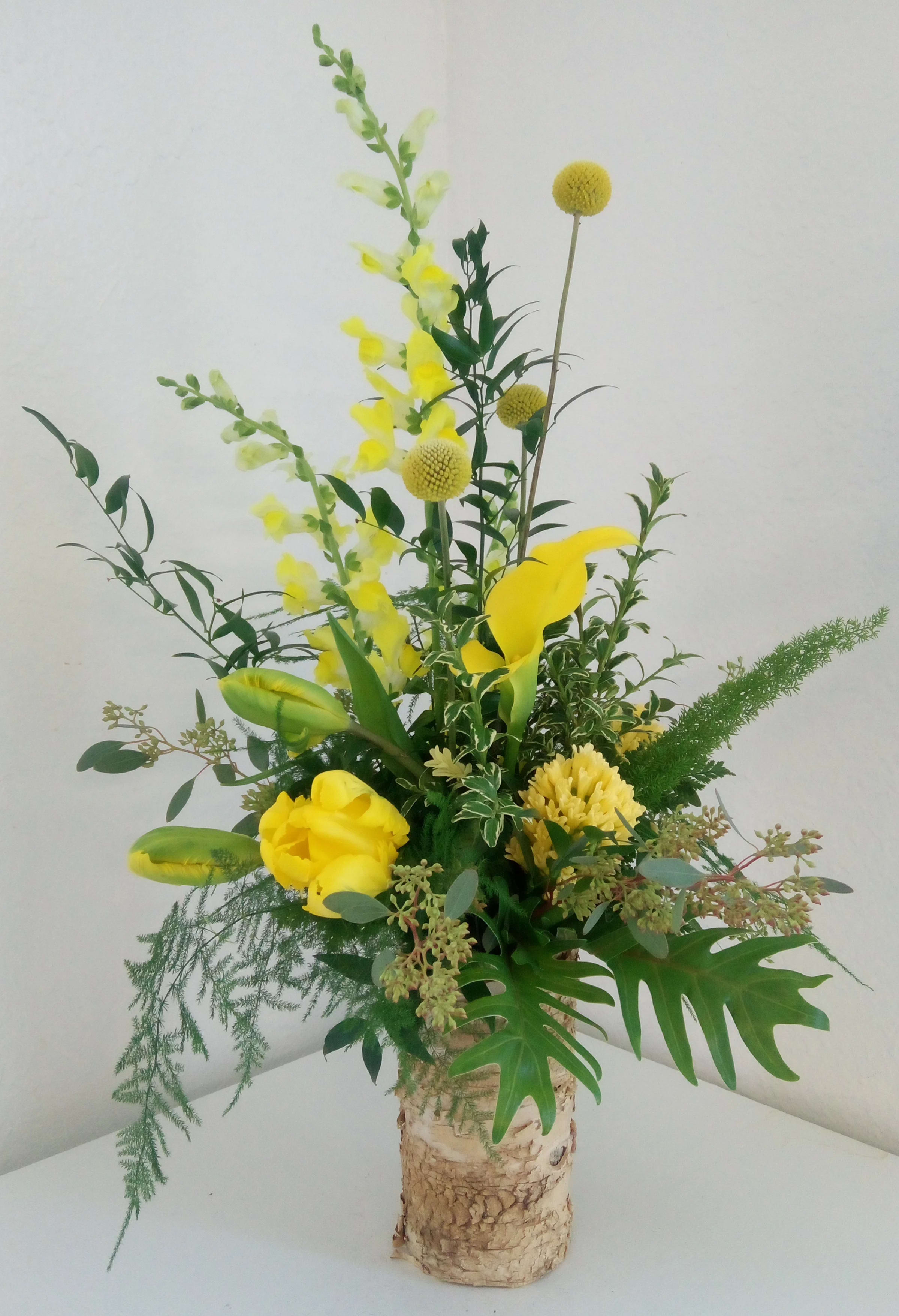 Sunny Daze - A bark covered cylinder filled with an assortment of greenery and shades of yellow flowers