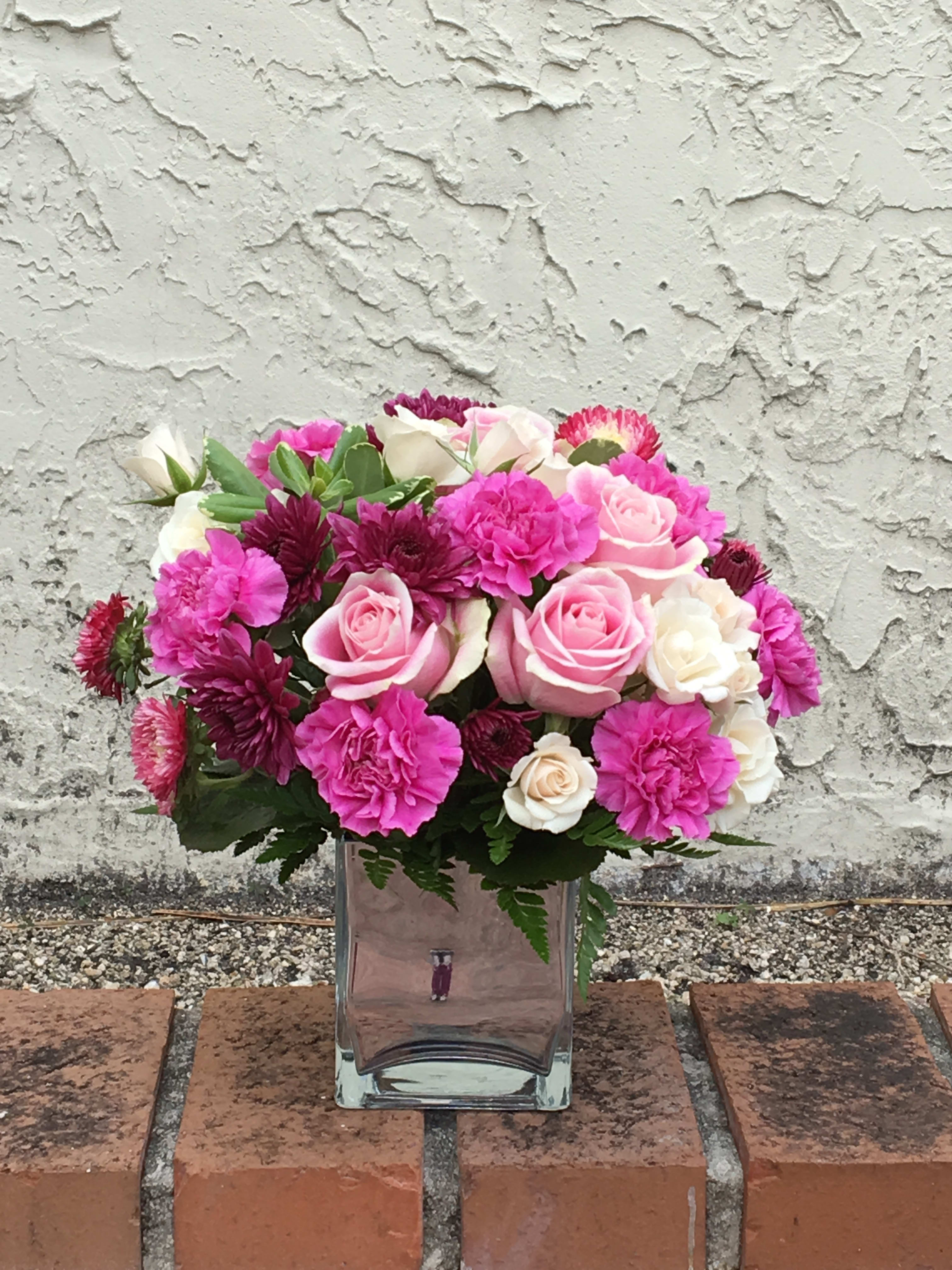 TREASURE HER - Show her just how treasured she is with this perfectly pink present. Hand-delivered in a classic cube vase, the chic mix of pale roses and hot pink blooms will make this day one to remember! Size: 11'' x 11H 